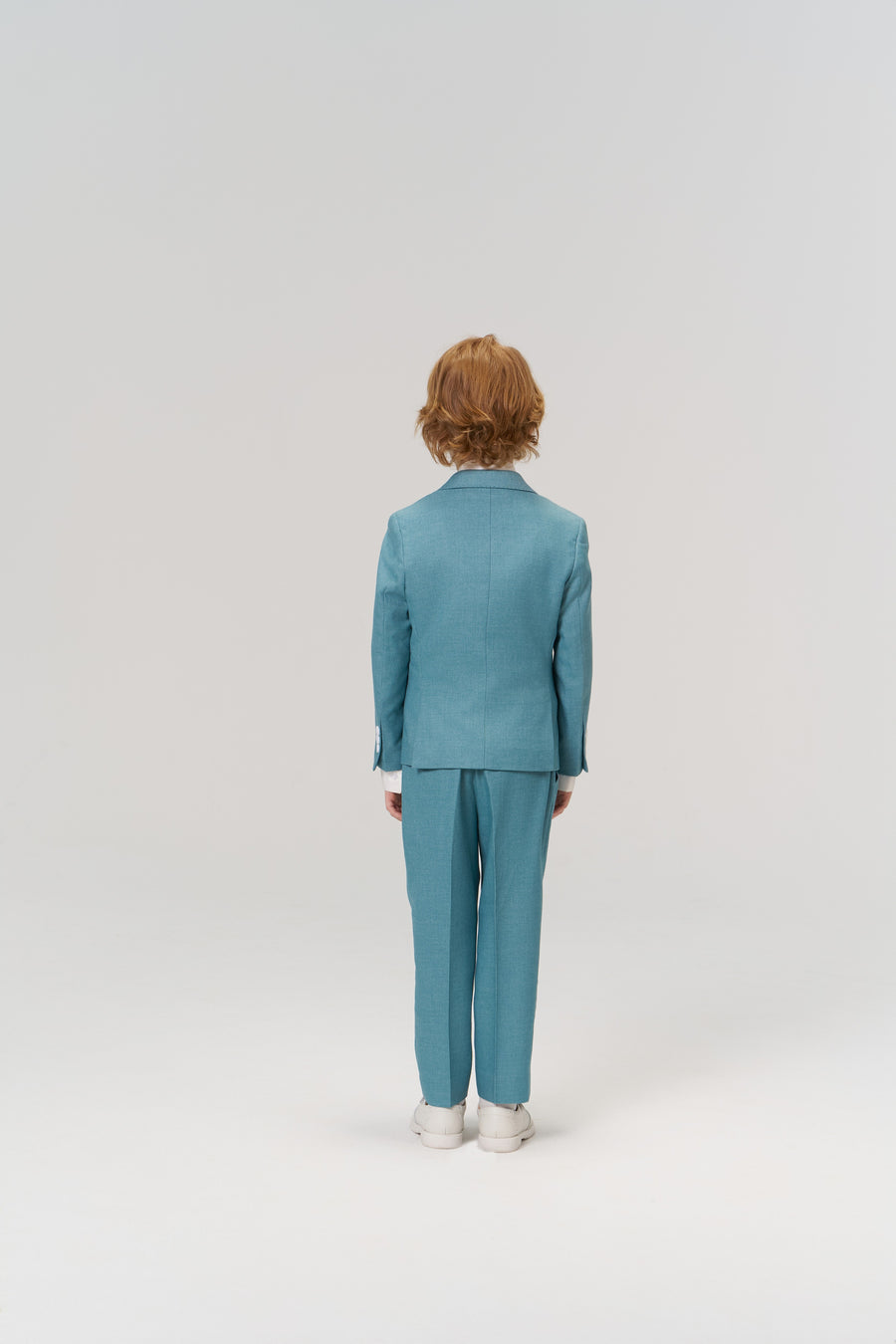 A child with red hair wears the KIKI and JOJO Celeste Whimsy Suit Jacket and white shoes, standing with their back to the camera against a plain light background.