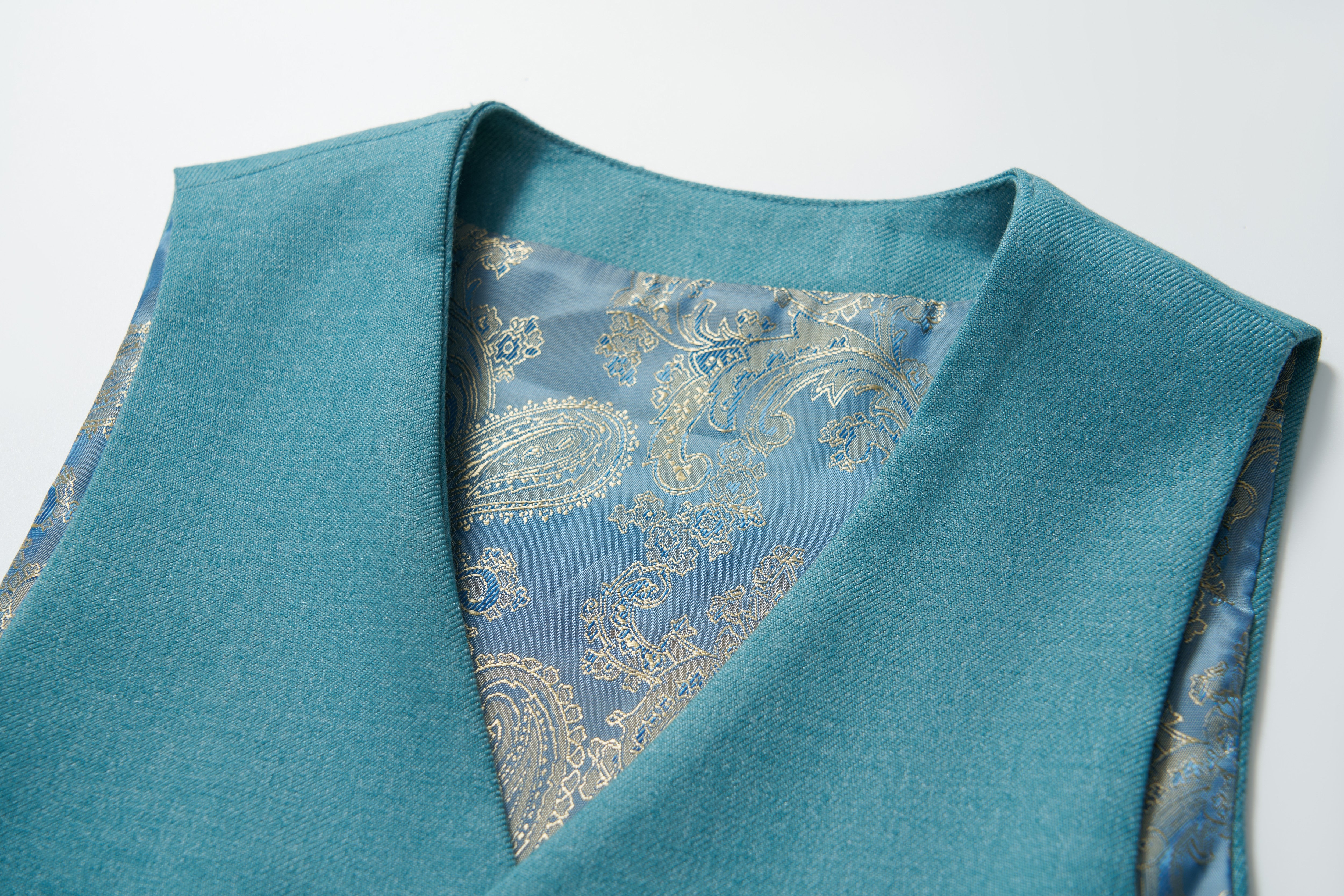 The Celeste Whimsy Suit Vest by KIKI and JOJO is a boys' peacock blue V-neck vest with a blue and gold paisley-patterned lining—ideal for a smart formal look.