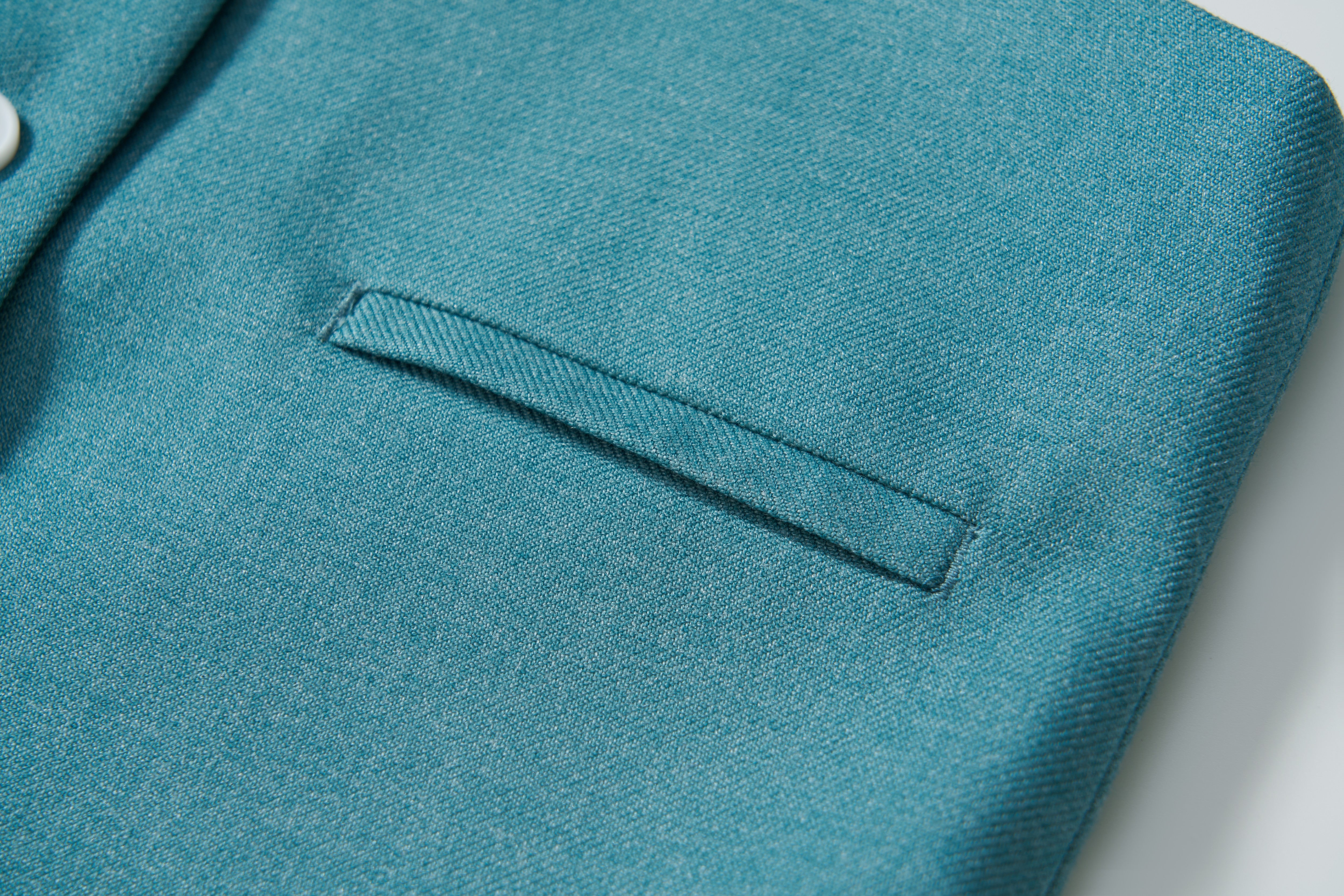 Close-up of the Celeste Whimsy Suit Vest by KIKI and JOJO in peacock blue, featuring a welt pocket and part of a button, ideal for formalwear, set against a light background.