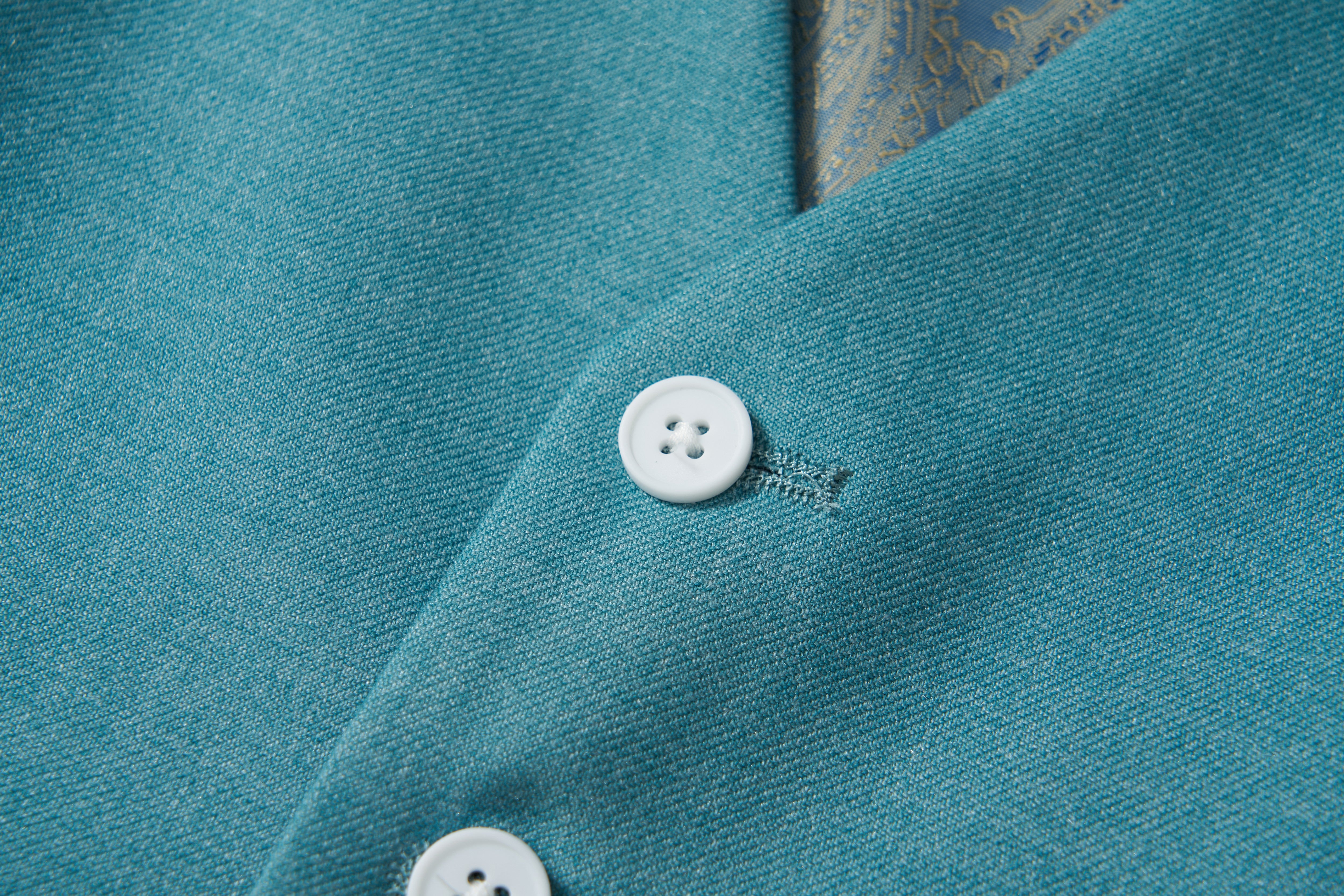 Close-up of two white buttons on peacock blue Celeste Whimsy Suit Vest by KIKI and JOJO, with patterned fabric in background—ideal for a sharp boys' formal look.