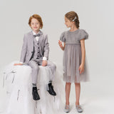 A young girl wearing KIKI and JOJO Girls Silver Bow Hair Clips stands in a gray dress next to a boy in a light gray suit, who sits on a white tulle-covered stool, both posed against a plain background.
