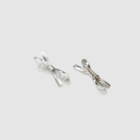 The KIKI and JOJO Girls Silver Bow Hair Clips - Set of 2 are shown on a light gray background, crafted from silver-toned PU leather, with one clip facing up and the other down to display both sides.