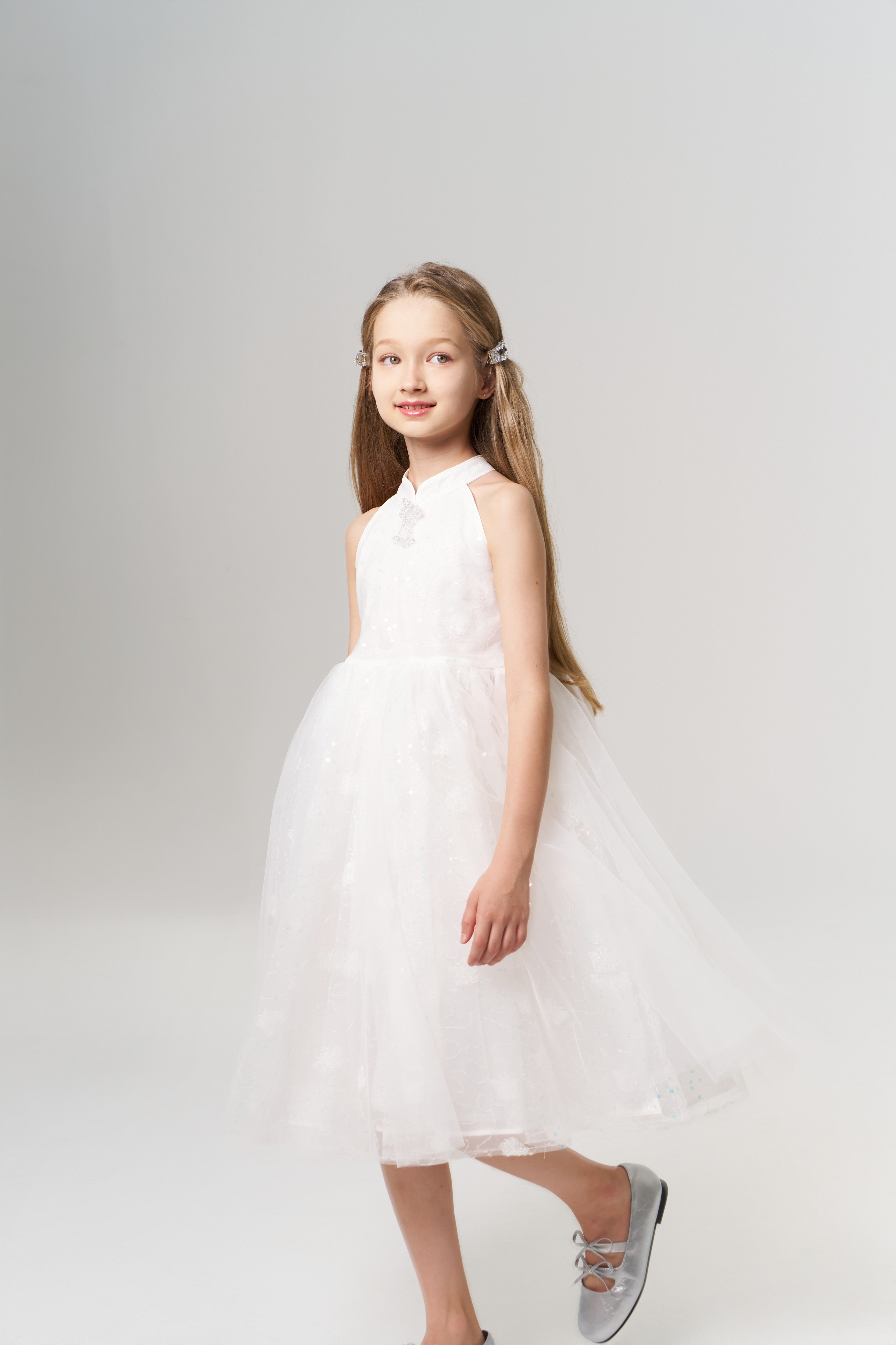 A young girl with long hair wears KIKI and JOJO's Girls Crystal Garden Barrettes (set of 2), a sleeveless white dress, and silver shoes, standing and smiling against a plain light background.