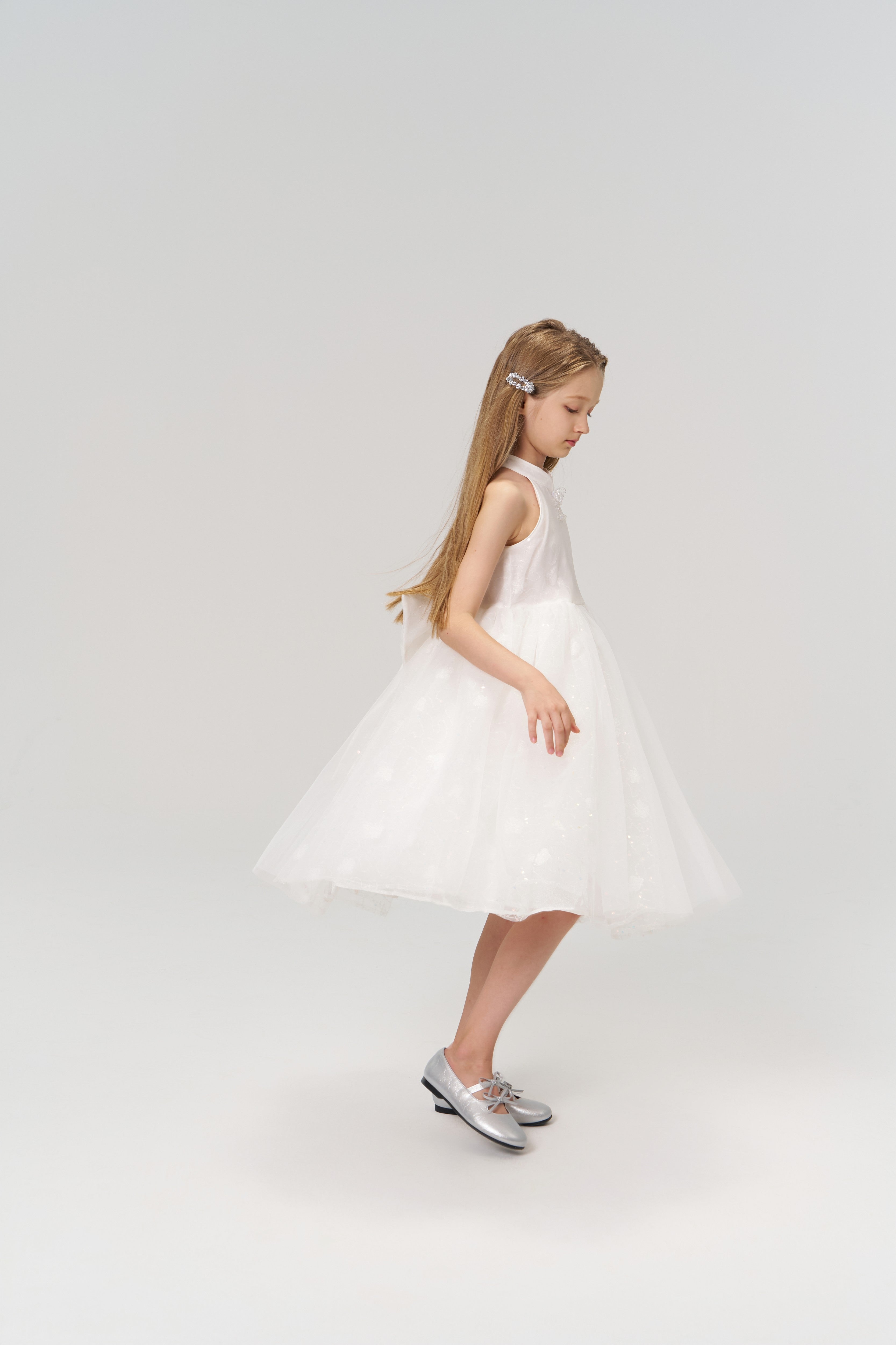A young girl with long hair wears KIKI and JOJO’s Girls Crystal Garden Barrettes (set of 2), a white sleeveless dress, and silver shoes, standing against a plain light background.