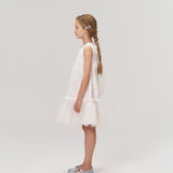 A young girl with long braided hair, styled with KIKI and JOJO’s Girls Crystal Garden Barrettes (set of 2), wears a sleeveless white dress and silver shoes, standing in profile against a plain light background.