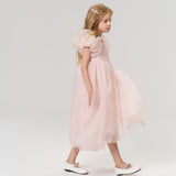 A young girl with long blonde hair, accessorized with KIKI and JOJO's Girls Pink Beaded Bow Hair Clips (Set of 2), walks left in a light pink dress and white shoes against a plain light background.