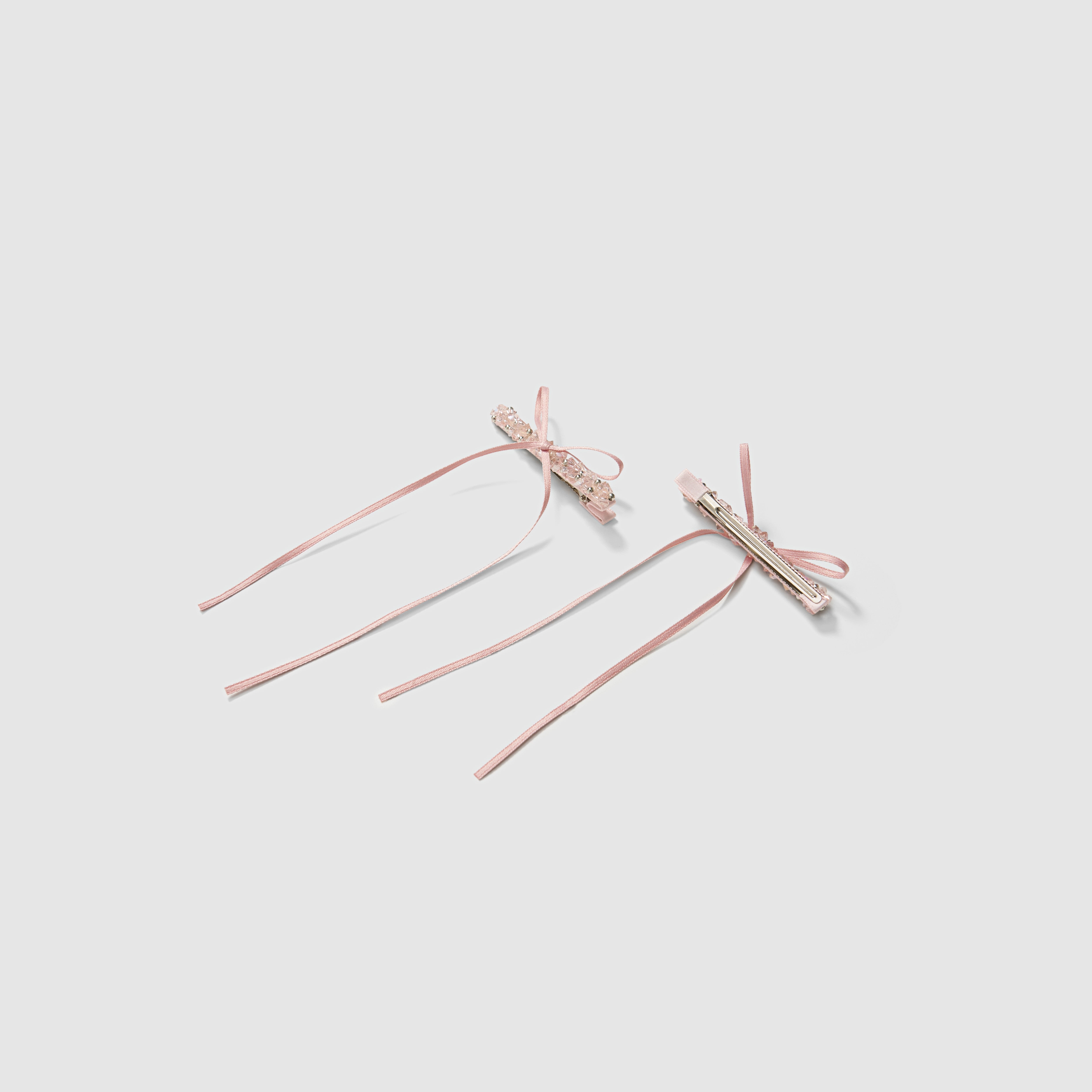 The KIKI and JOJO Girls Pink Beaded Bow Hair Clips, set of 2, are shown on a light grey background—one displays the beaded bow front, the other shows the metal clasp. These clips bring a soft, elegant touch to any hairstyle.