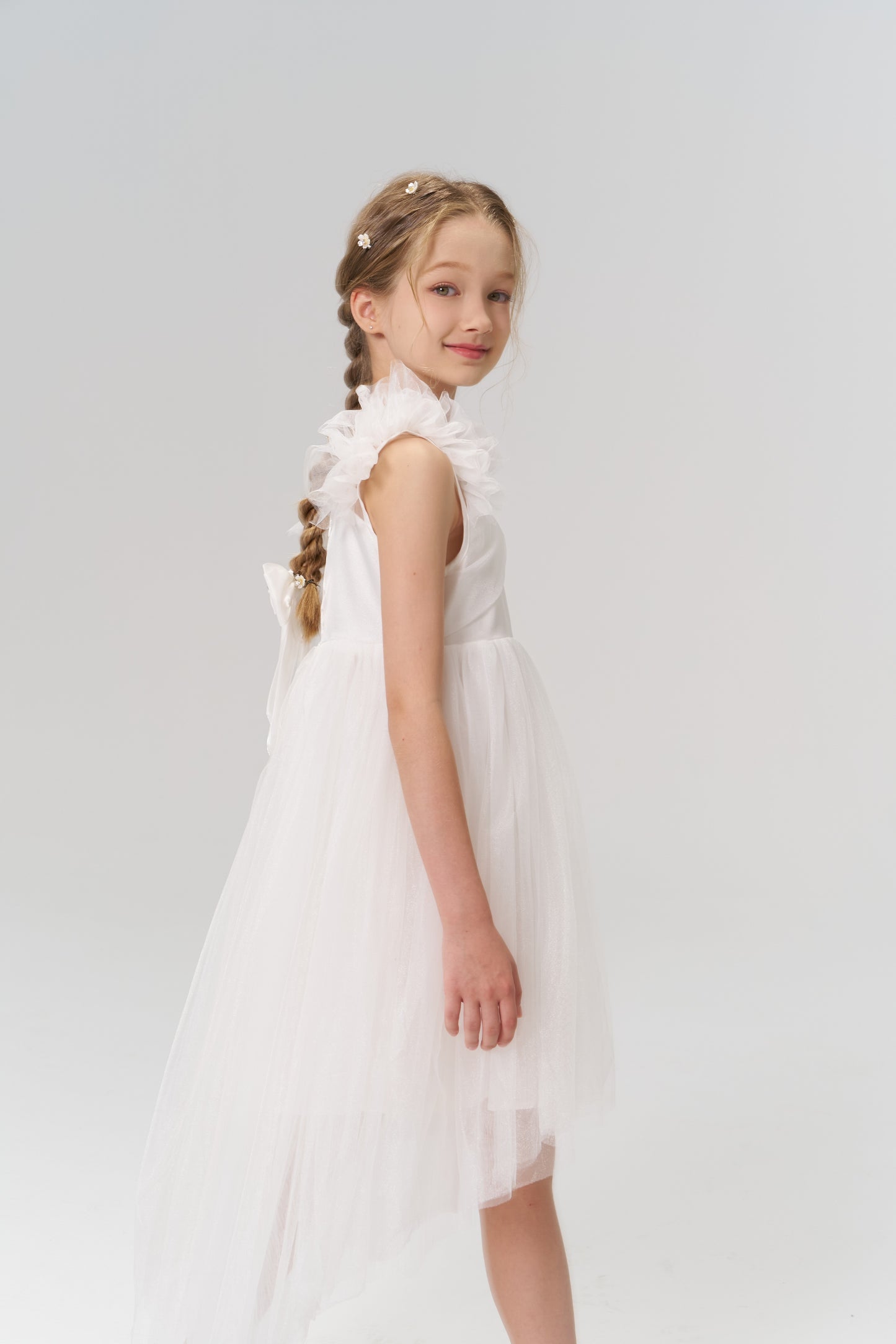 A young girl with braided hair wears KIKI and JOJO's Girls Daisy Crystal Flower Hair Clips (set of 6) and a white ruffled dress, standing sideways and looking at the camera against a plain light background.