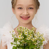 A young blonde girl in a white dress smiles at the camera, holding a bouquet and wearing KIKI and JOJO's Girls Daisy Crystal Flower Hair Clips (Set of 6)—the perfect flower girl hair accessories—against a plain background.