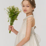 A young girl wears KIKI and JOJO's Girls Daisy Crystal Flower Hair Clips (Set of 6) in her hair, paired with a white dress and a bouquet of yellow and white flowers, standing against a plain light background.
