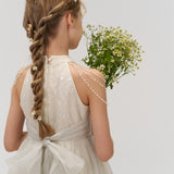 A girl with braided hair, styled with KIKI and JOJO Girls Daisy Crystal Flower Hair Clips (Set of 6), wears a white dress with a bow and holds a bouquet of yellow and white flowers, facing away from the camera.