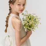 A young girl in a white dress, her braids styled with KIKI and JOJO’s Girls Daisy Crystal Flower Hair Clips (Set of 6), holds a bouquet of small white and yellow flowers against a plain light background.
