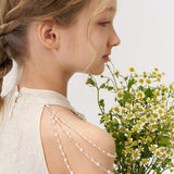 A young girl with braided hair styled with KIKI and JOJO’s Girls Daisy Crystal Flower Hair Clips (set of 6) wears a cream dress and beaded shoulder accessory, holding chamomile flowers as she looks to the side.