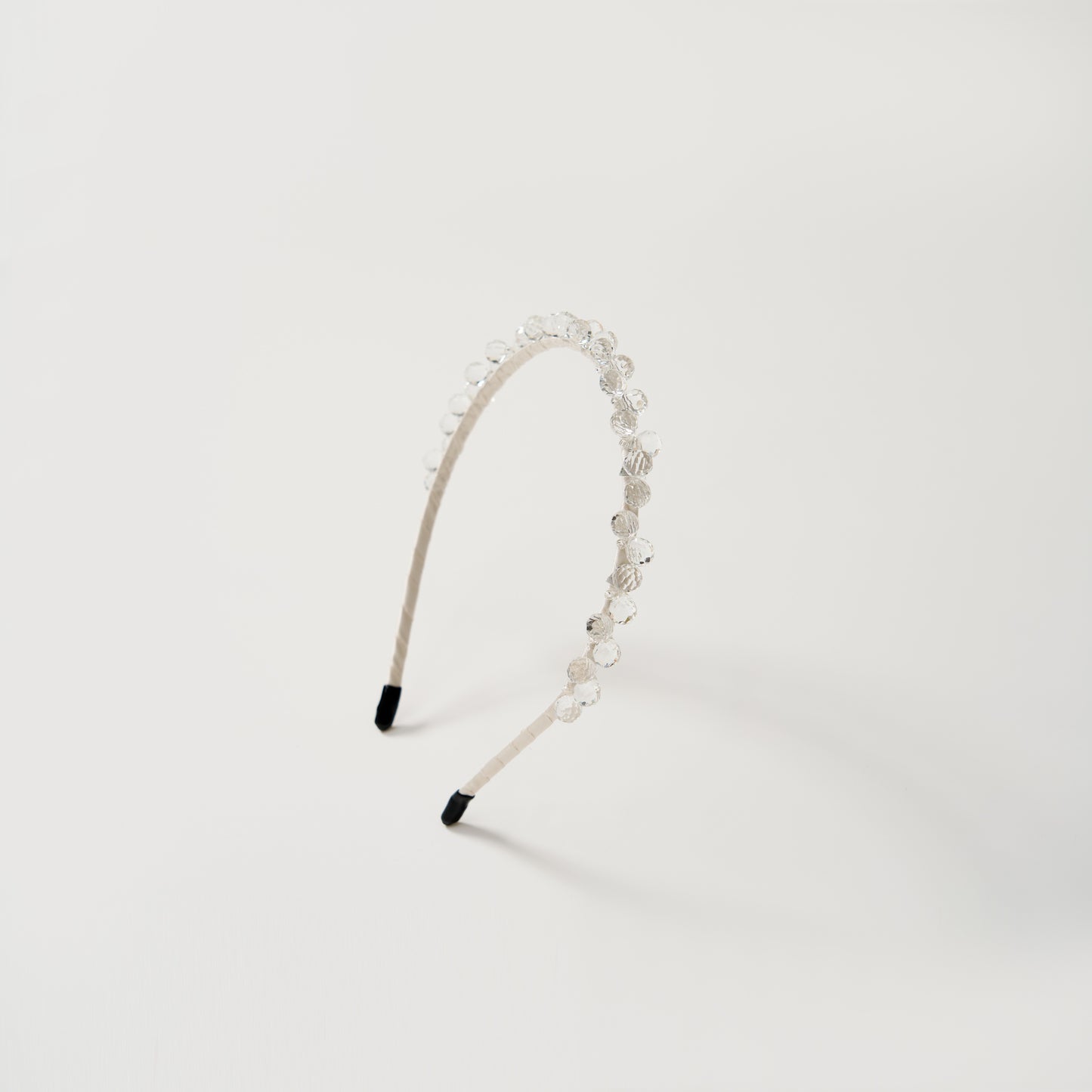 The KIKI and JOJO Girls Crystal Bead Headband, shown on a plain white background, features a beige band adorned with small clear beads—an elegant accessory for flower girls.