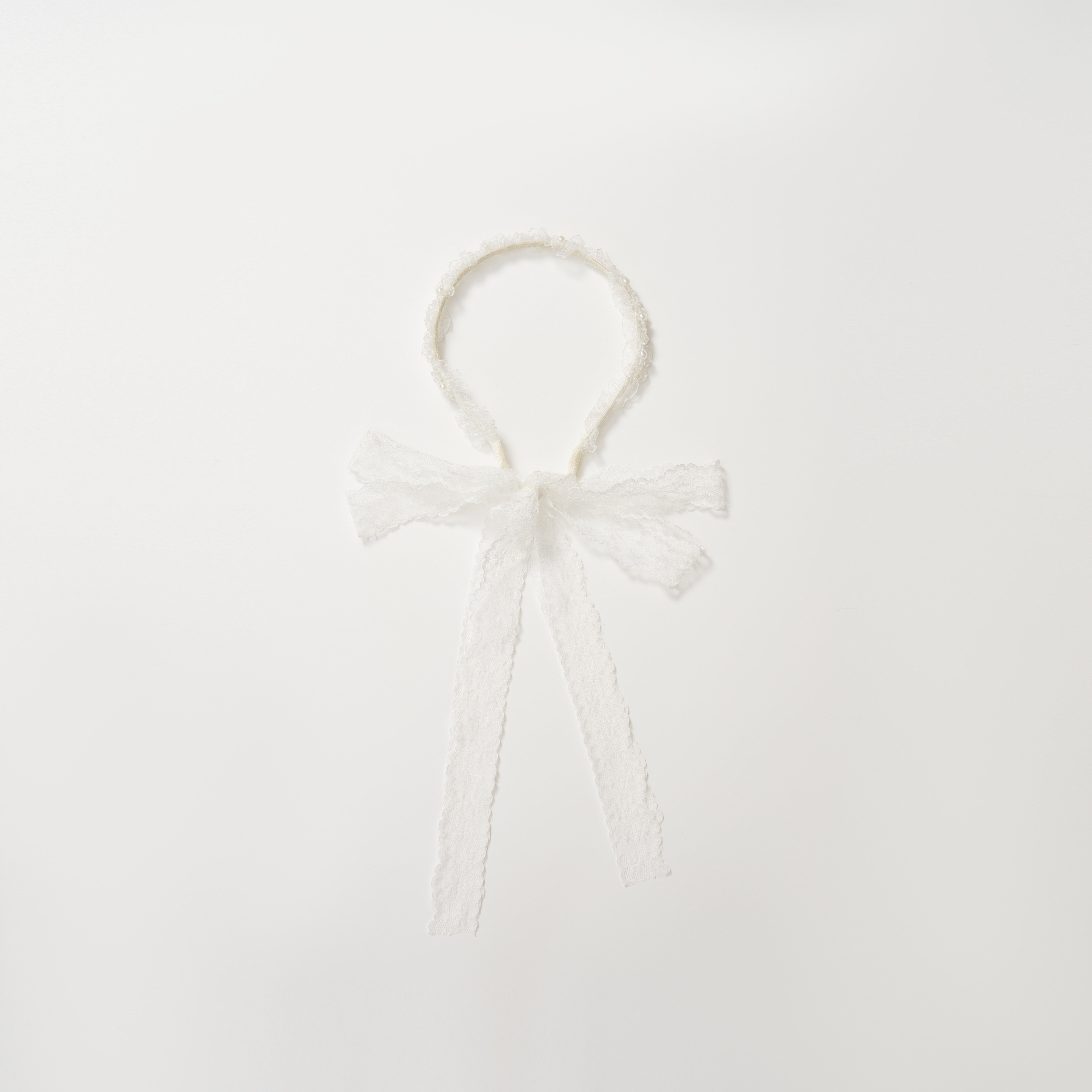 The KIKI and JOJO Girls Pearl Lace Ribbon Headband features white lace, a sweet bow, and long ribbons—an ideal flower girl accessory. Shown on a plain white background.