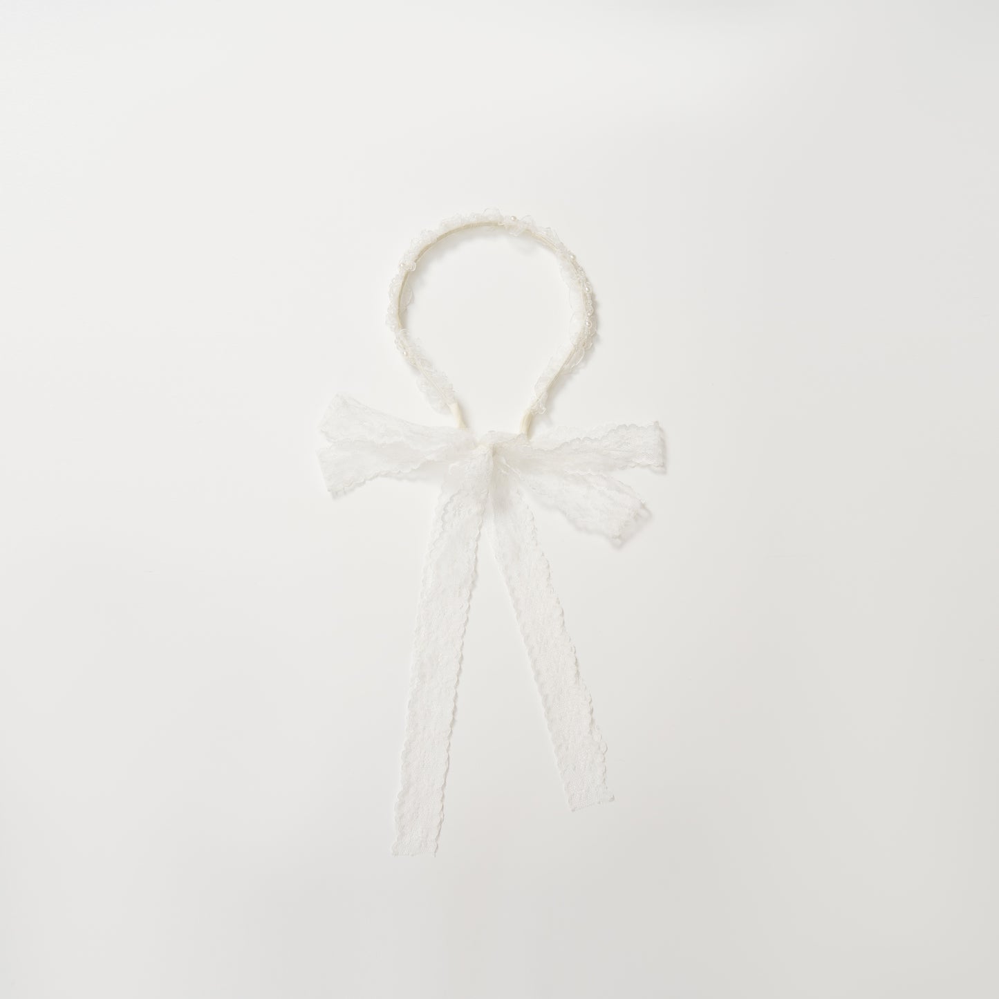 The KIKI and JOJO Girls Pearl Lace Ribbon Headband features white lace, a sweet bow, and long ribbons—an ideal flower girl accessory. Shown on a plain white background.