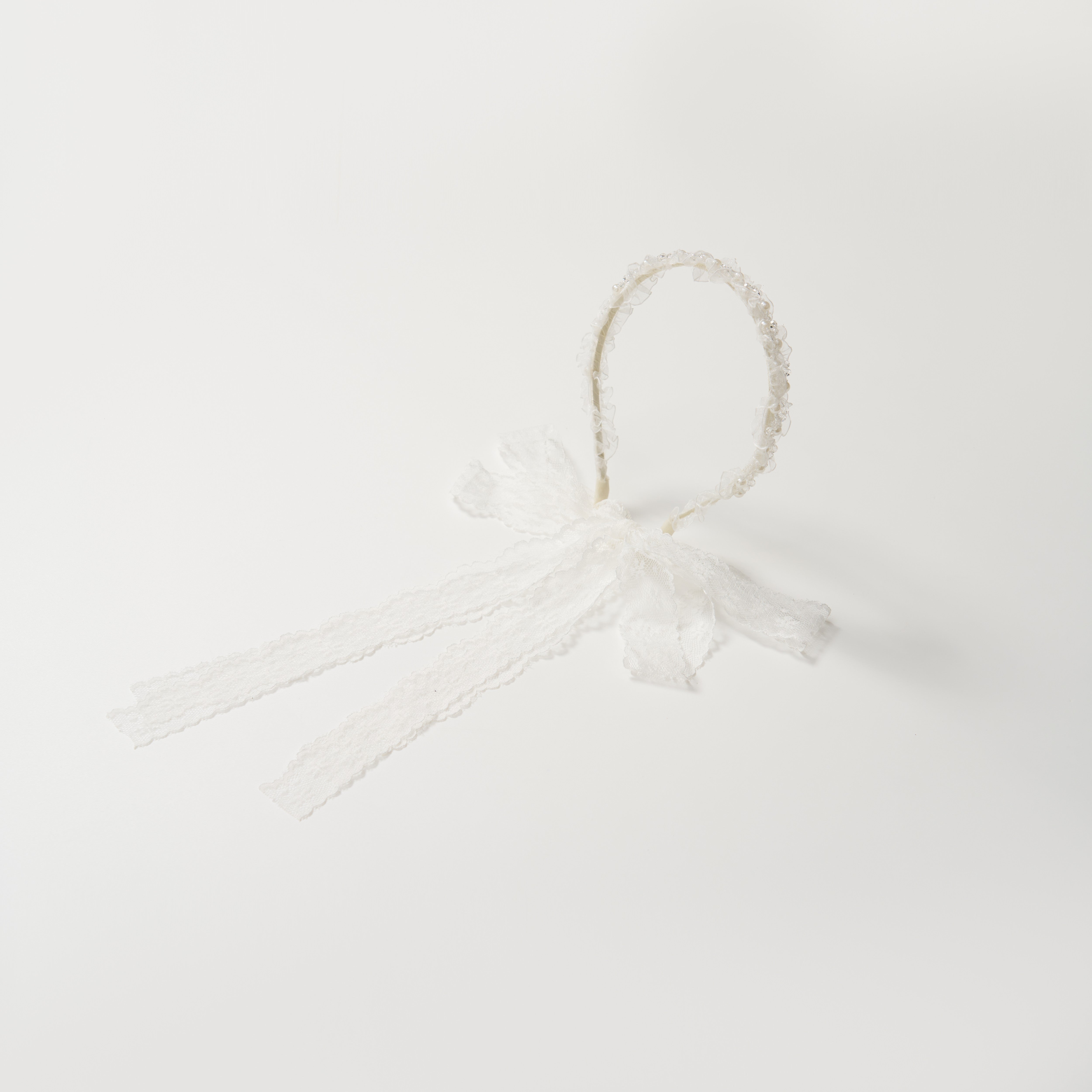 The KIKI and JOJO Girls Pearl Lace Ribbon Headband features white lace, a decorative bow, and two long lace ribbons—ideal for a flower girl accessory. Shown on a plain white background.