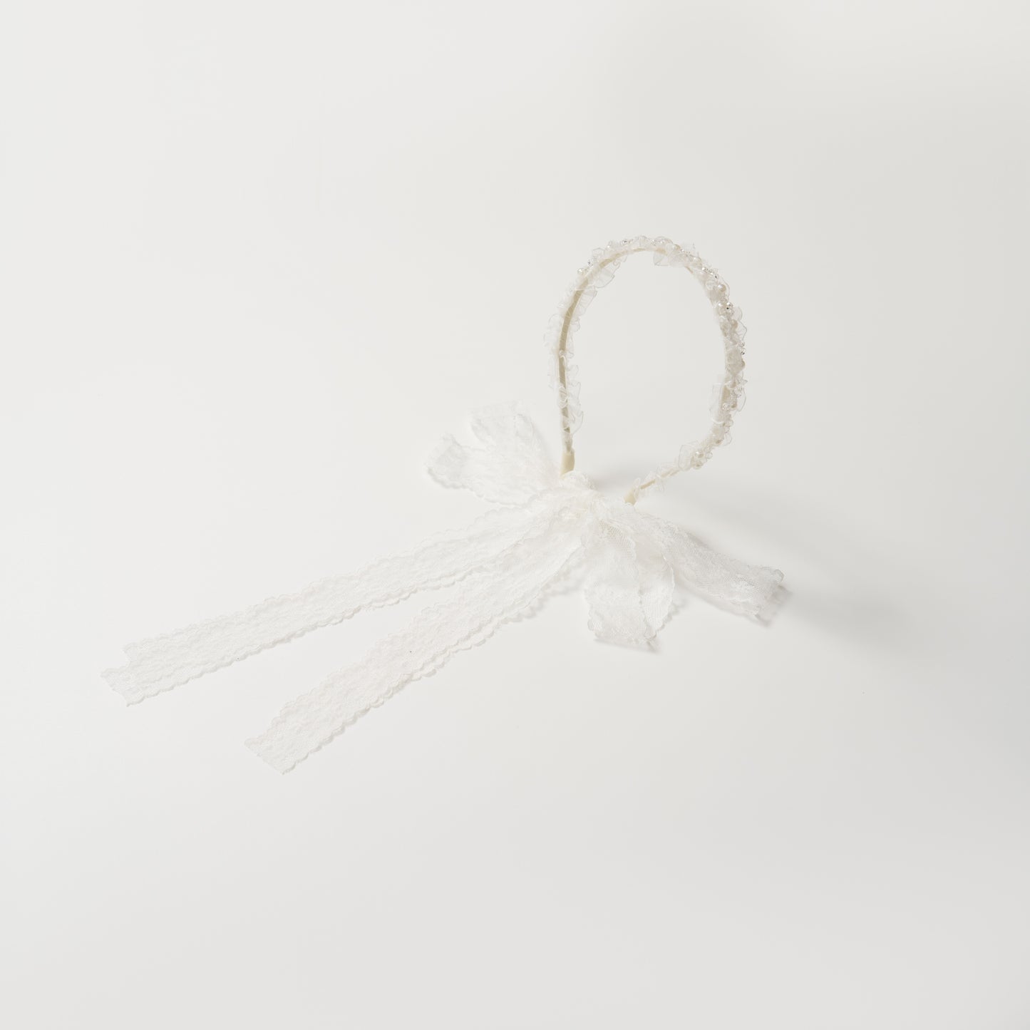 The KIKI and JOJO Girls Pearl Lace Ribbon Headband features white lace, a decorative bow, and two long lace ribbons—ideal for a flower girl accessory. Shown on a plain white background.