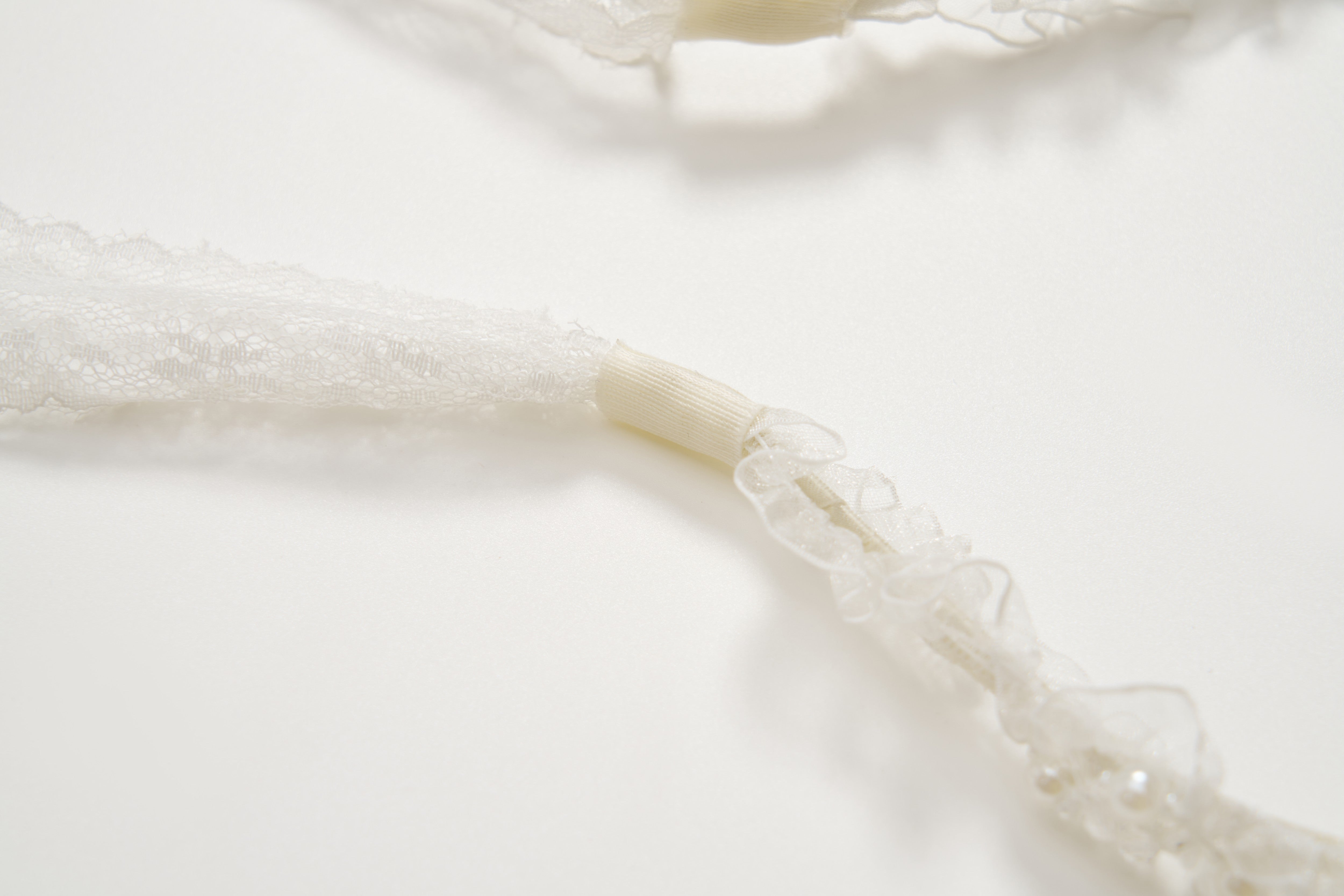 Close-up of white lace straps with elastic sections on a plain background—an elegant detail from the KIKI and JOJO Girls Pearl Lace Ribbon Headband, ideal as a flower girl accessory or paired with handcrafted pieces.