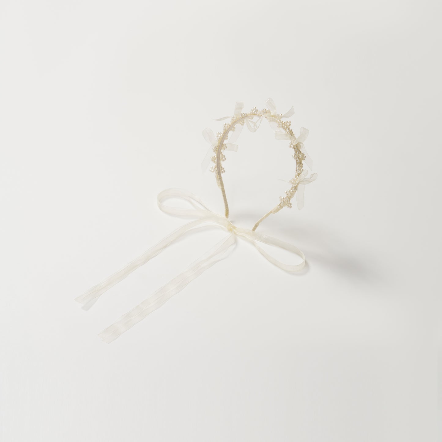 The KIKI and JOJO Girls Pearl Bow Crown Headband features delicate pearls and an elegant white bow, presented against a plain white background.