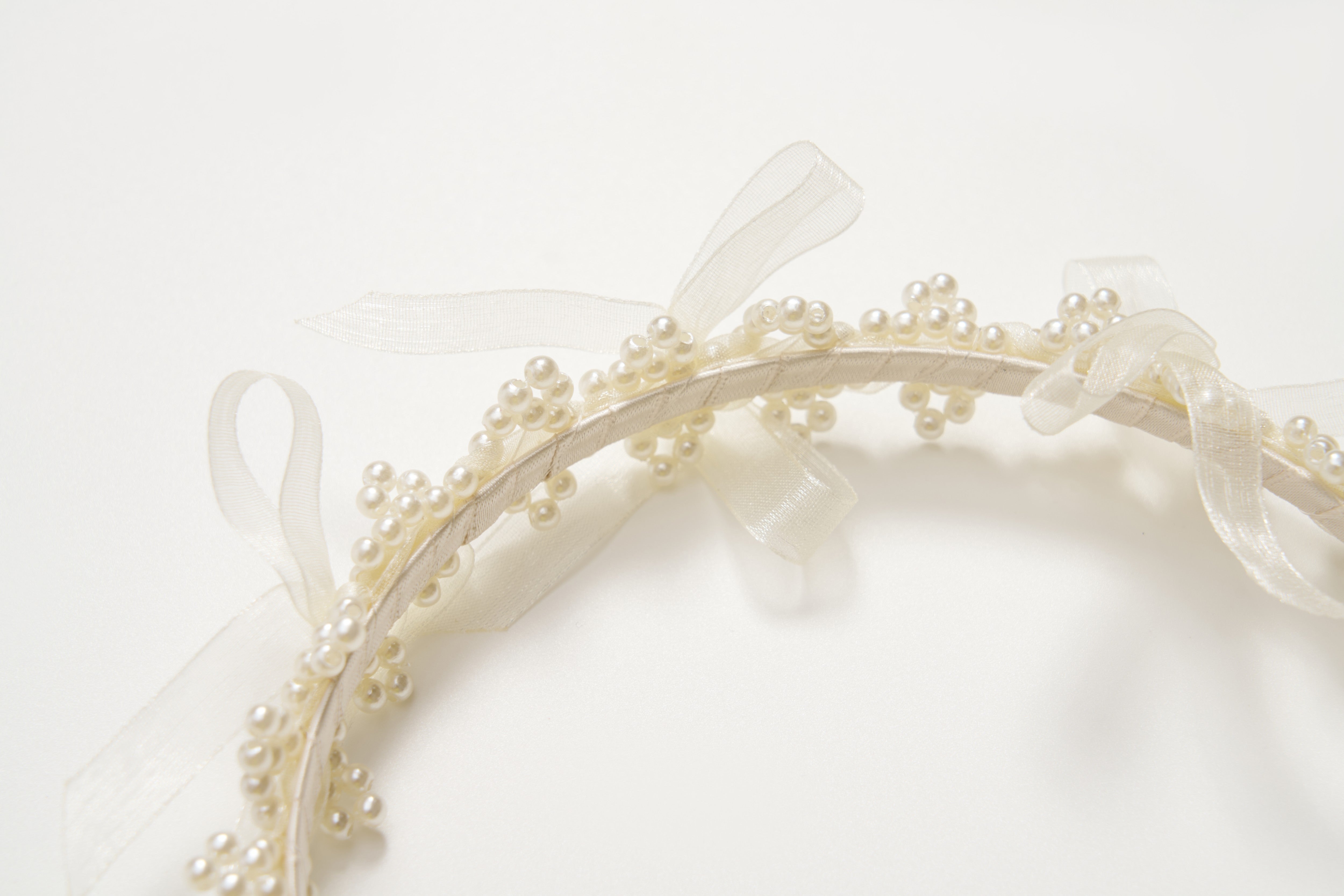 The KIKI and JOJO Girls Pearl Bow Crown Headband features small white pearls and sheer organza bows, shown in close-up against a white background.