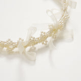 A close-up of the KIKI and JOJO Girls Pearl Bow Crown Headband, adorned with white pearls and sheer organza bows, displayed against a white background.