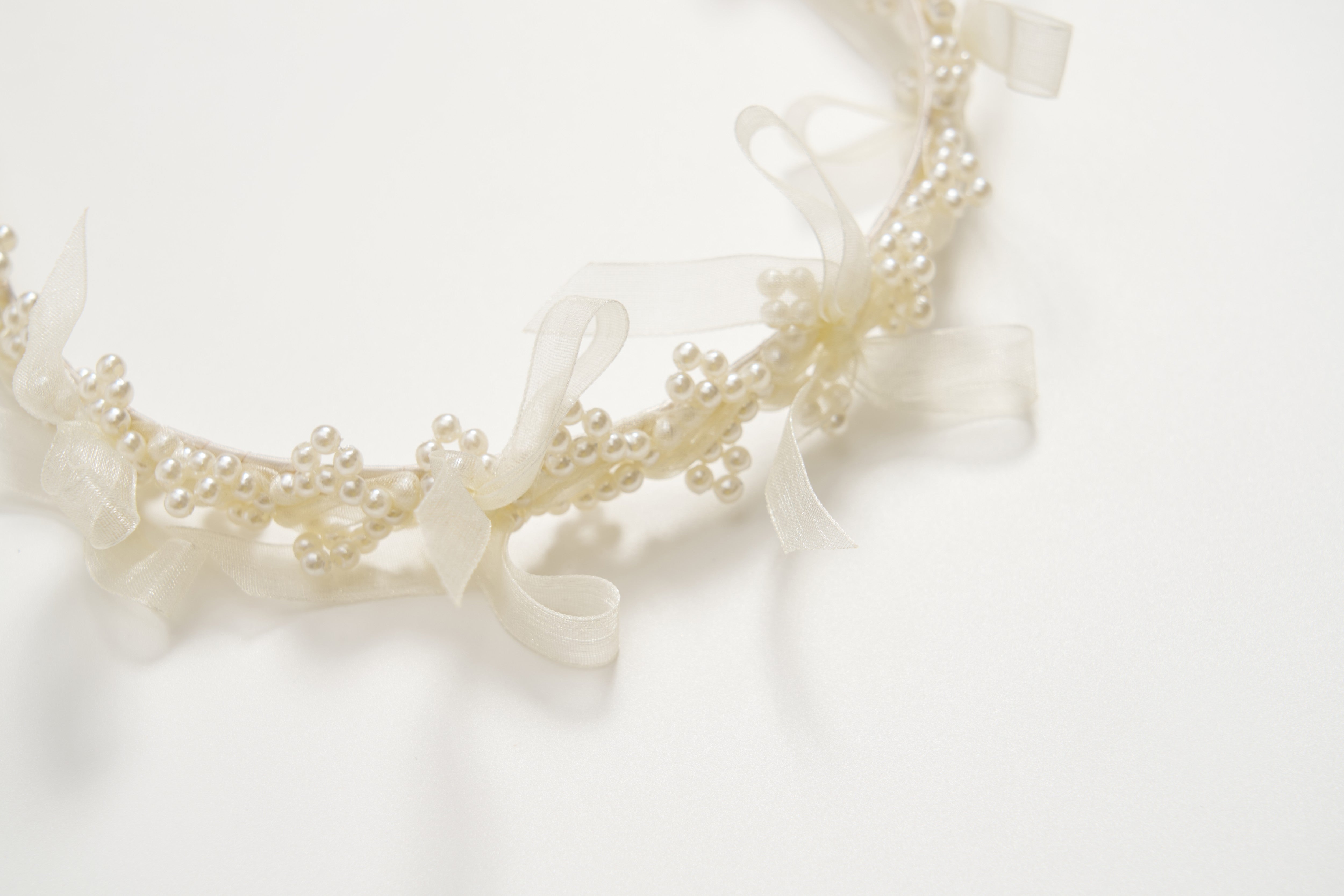 A close-up of the KIKI and JOJO Girls Pearl Bow Crown Headband, adorned with white pearls and sheer organza bows, displayed against a white background.
