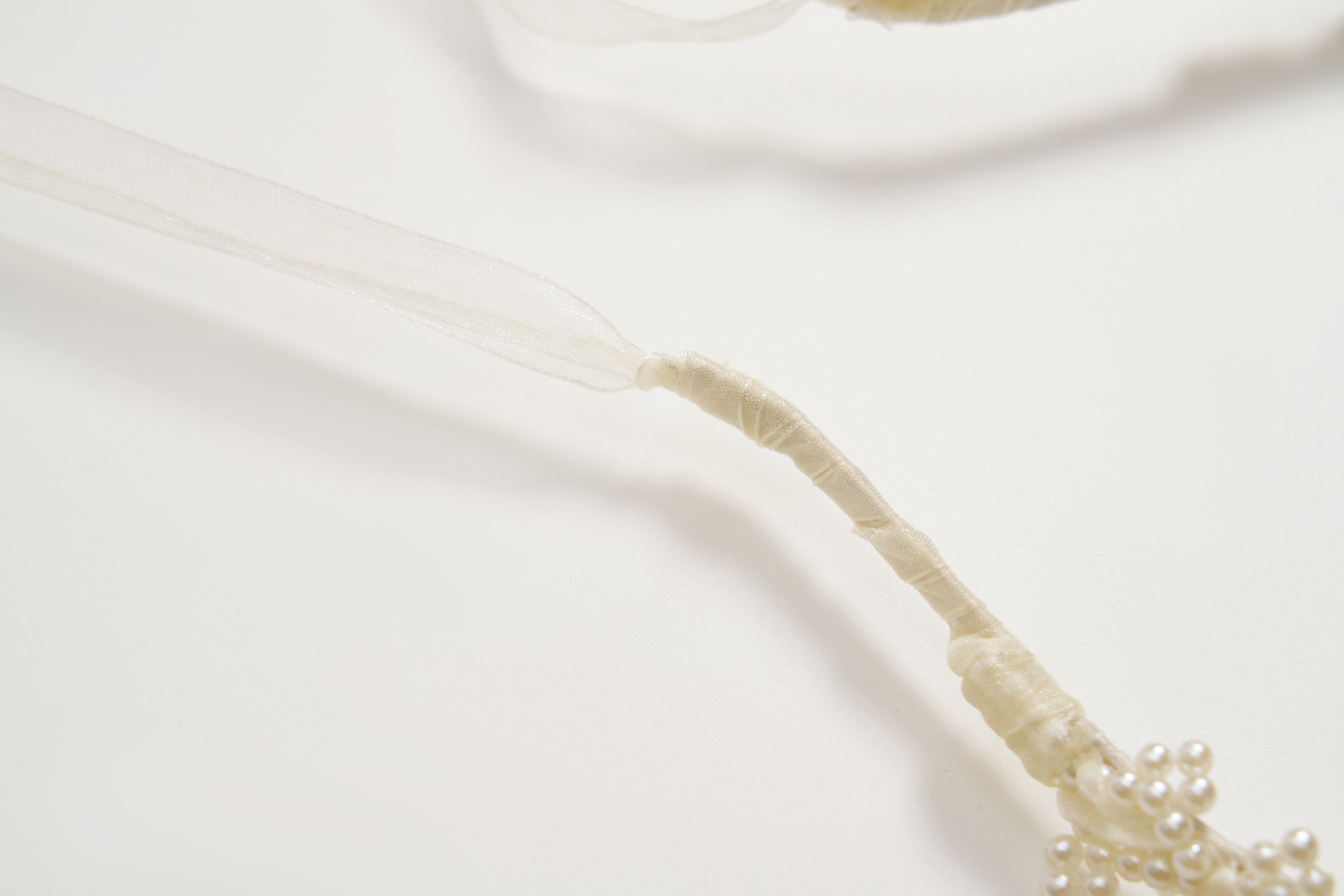 The KIKI and JOJO Girls Pearl Bow Crown Headband features beige wrapping, white ribbon, faux pearl clusters like a pearl crown, and organza bows, all shown in close-up on a white background.