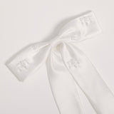 The Girls Hand-Beaded Pearl Satin Bow Hair Clip by KIKI and JOJO features embroidered patterns and beaded details on each loop and tail, making it a perfect flower girl accessory. Shown against a light plain background.