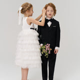 A girl wearing the KIKI and JOJO Girls Hand-Beaded Pearl Satin Bow Hair Clip adjusts a boy’s hair as he holds a bouquet; both are dressed formally against a plain background.