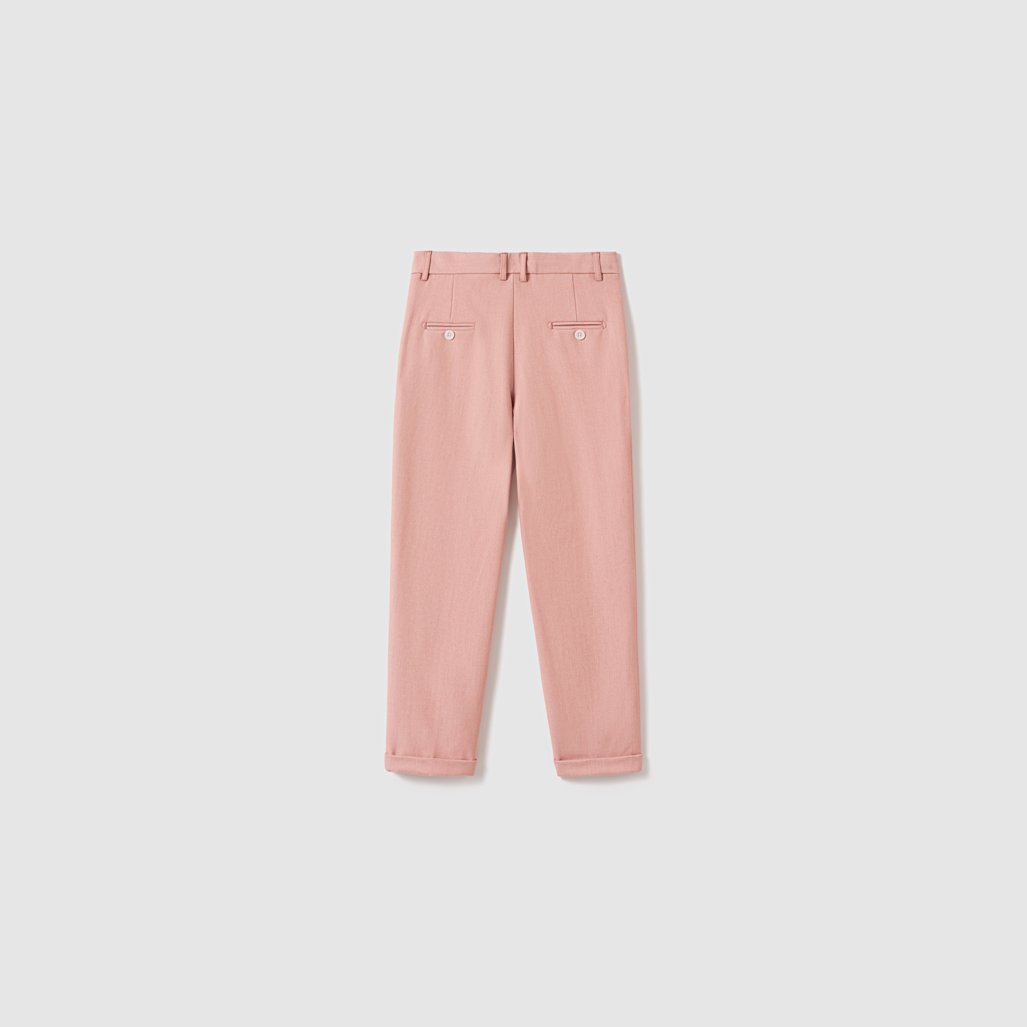 The Blush Reverie Suit Pants by KIKI and JOJO are blush pink boys' trousers featuring belt loops, an adjustable waistband, two buttoned back pockets, and neatly folded cuffs, displayed flat on a white background.