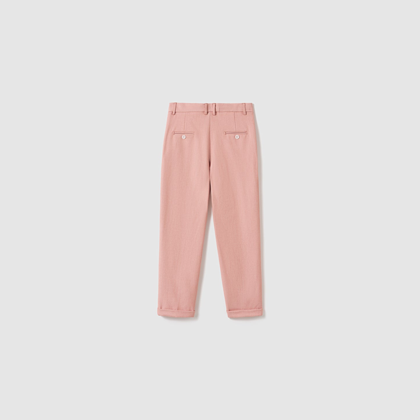 The Blush Reverie Suit Pants by KIKI and JOJO are blush pink boys' trousers featuring belt loops, an adjustable waistband, two buttoned back pockets, and neatly folded cuffs, displayed flat on a white background.