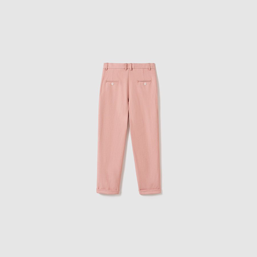 The Blush Reverie Suit Pants by KIKI and JOJO are blush pink boys' trousers featuring belt loops, an adjustable waistband, two buttoned back pockets, and neatly folded cuffs, displayed flat on a white background.
