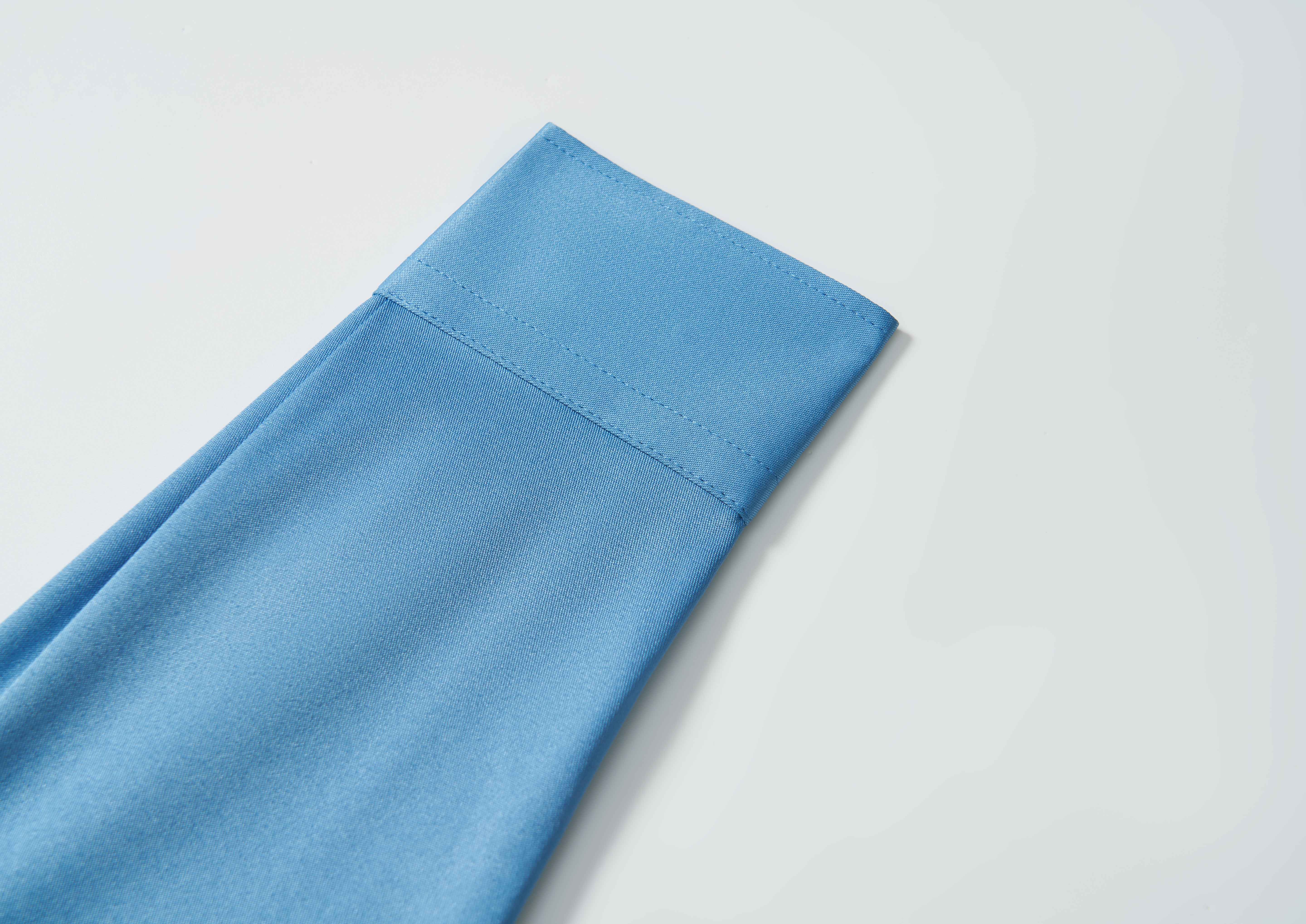 A close-up of the KIKI and JOJO Boys Sky Blue Dress Shirt, neatly folded with visible stitching, displayed on a white background.