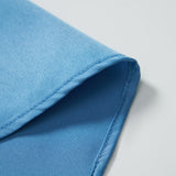 A close-up of the corner of the KIKI and JOJO Boys Sky Blue Dress Shirt highlights its crisp fabric, neatly folded on a white surface.