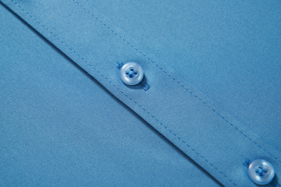 Close-up of KIKI and JOJO Boys Sky Blue Dress Shirt fabric, featuring visible stitching and two plastic buttons on the placket.