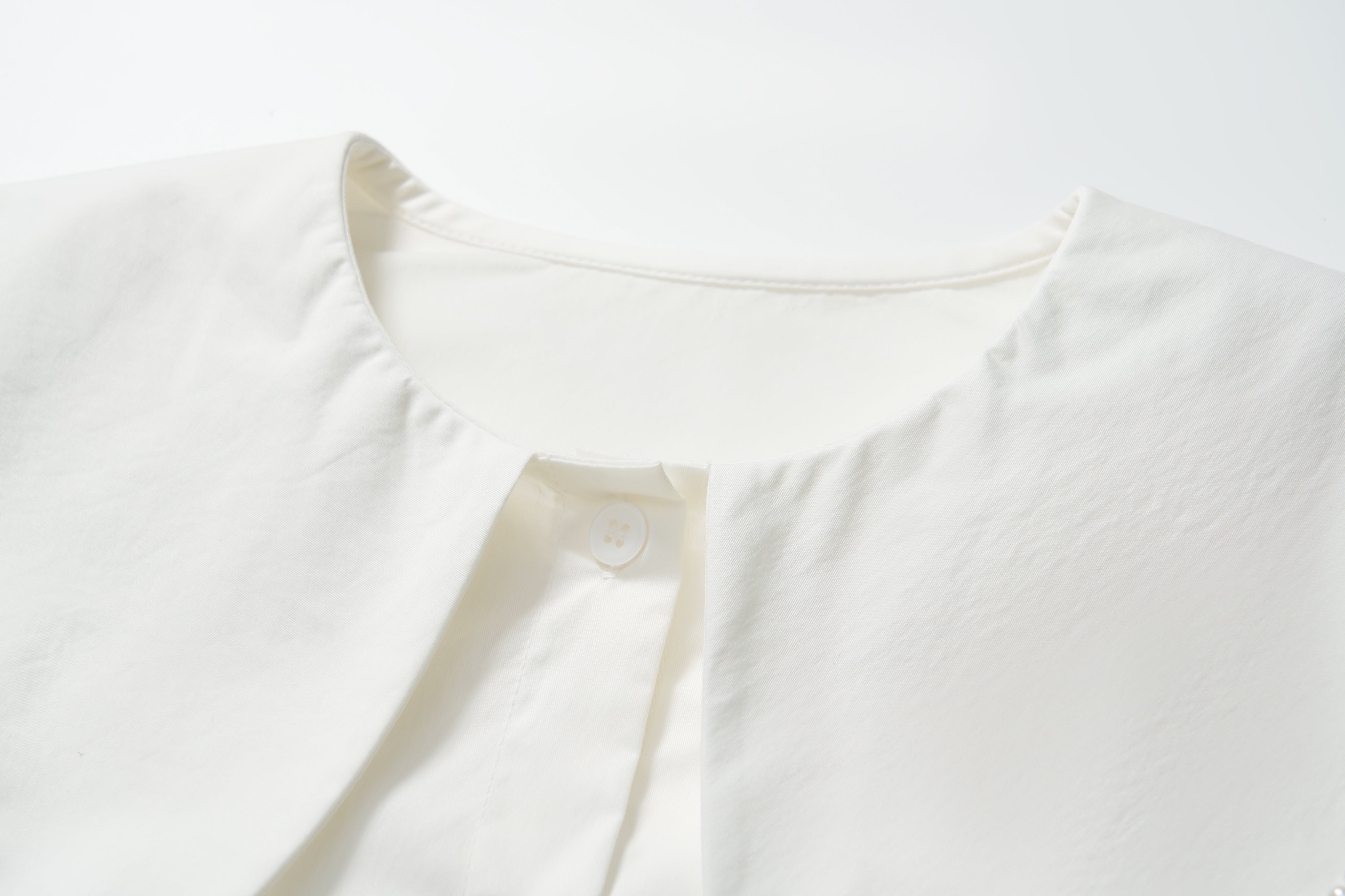 Close-up of the scalloped collar and top button of the Moonlit Whisper Blouse by KIKI and JOJO, a vintage-inspired white blouse laid flat on a white surface.