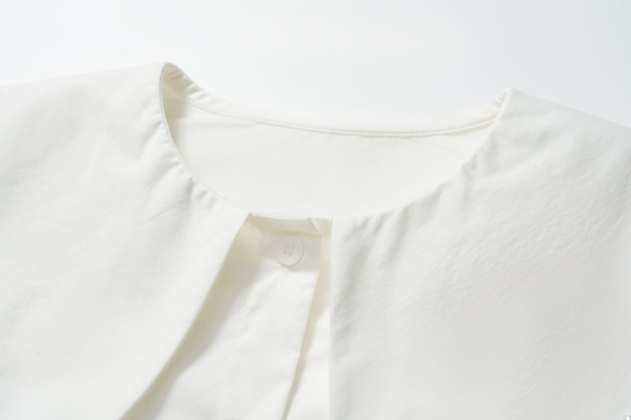 Close-up of the scalloped collar and top button of the Moonlit Whisper Blouse by KIKI and JOJO, a vintage-inspired white blouse laid flat on a white surface.