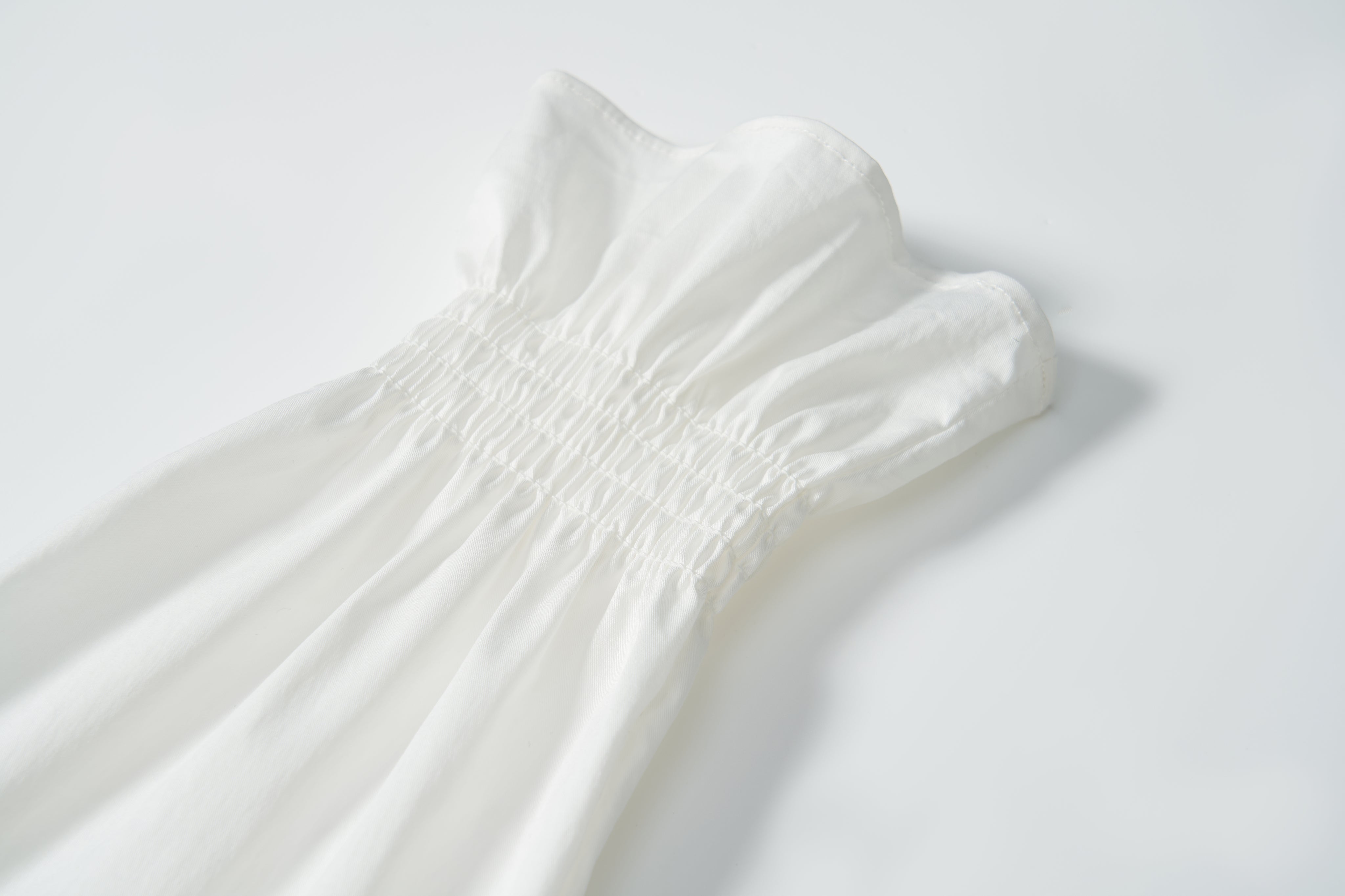 Close-up of the Moonlit Whisper Blouse by KIKI and JOJO, featuring gathered elastic smocking at the waist and a ruffled top trim, laid flat on a white background.