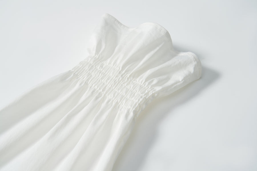 Close-up of the Moonlit Whisper Blouse by KIKI and JOJO, featuring gathered elastic smocking at the waist and a ruffled top trim, laid flat on a white background.