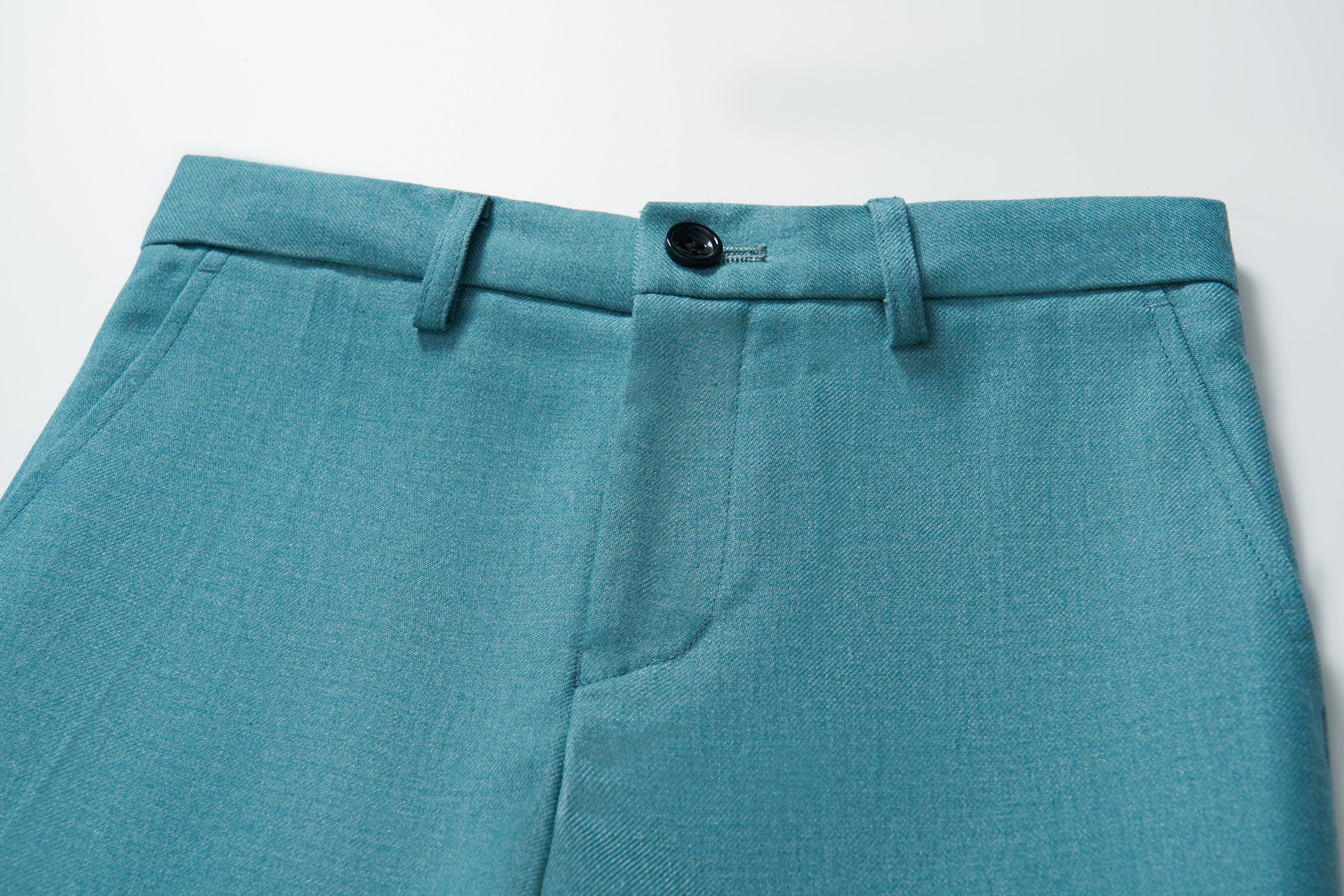 Close-up of KIKI and JOJO’s Celeste Whimsy Suit Pants for boys in turquoise, showcasing a button closure, belt loops, adjustable waistband, and front seam detail on a white background.