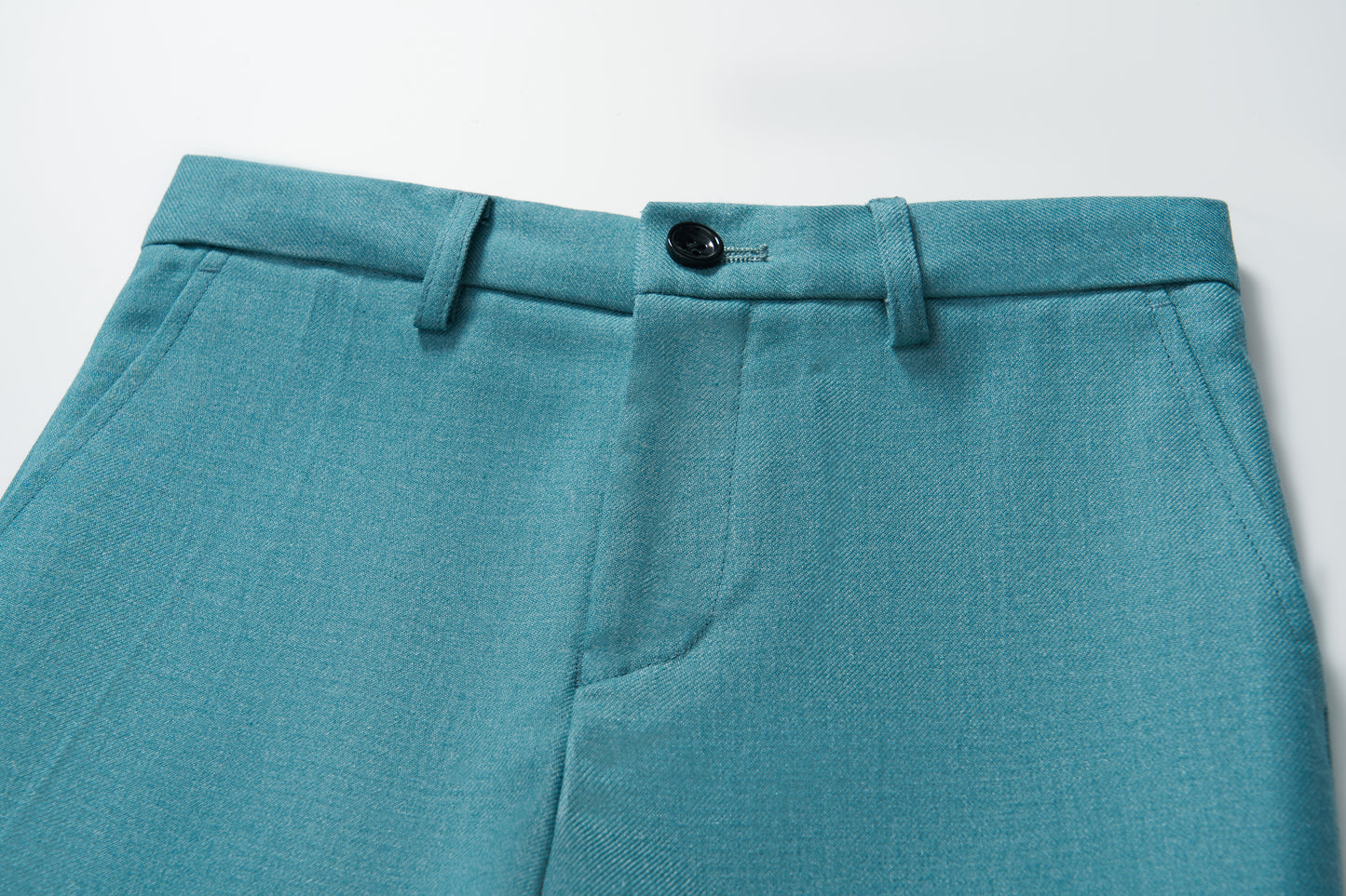 Close-up of KIKI and JOJO’s Celeste Whimsy Suit Pants for boys in turquoise, showcasing a button closure, belt loops, adjustable waistband, and front seam detail on a white background.