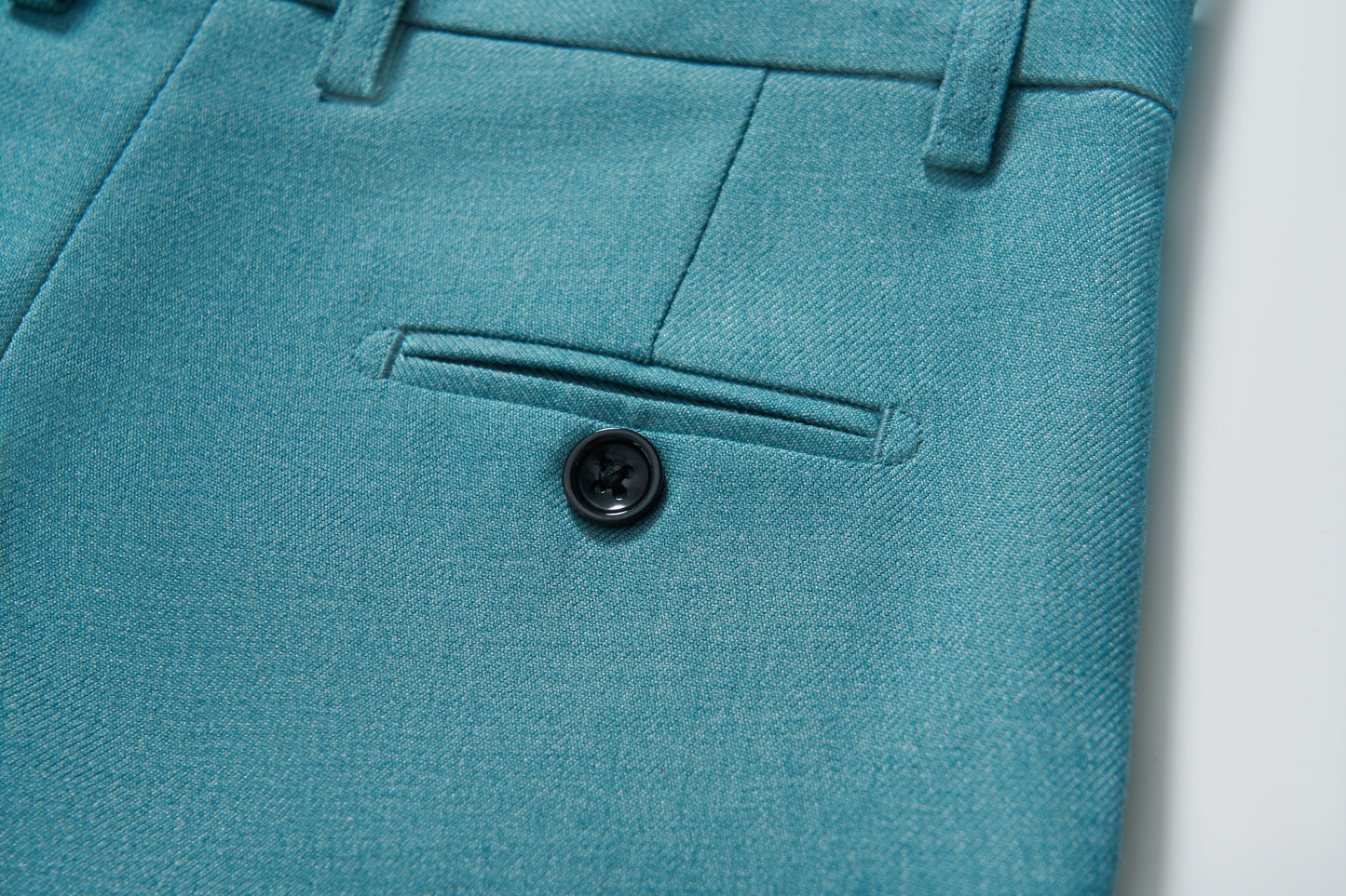 Close-up of the turquoise pocket with button on KIKI and JOJO's Celeste Whimsy Suit Pants for boys, featuring an adjustable waistband for a perfect fit.