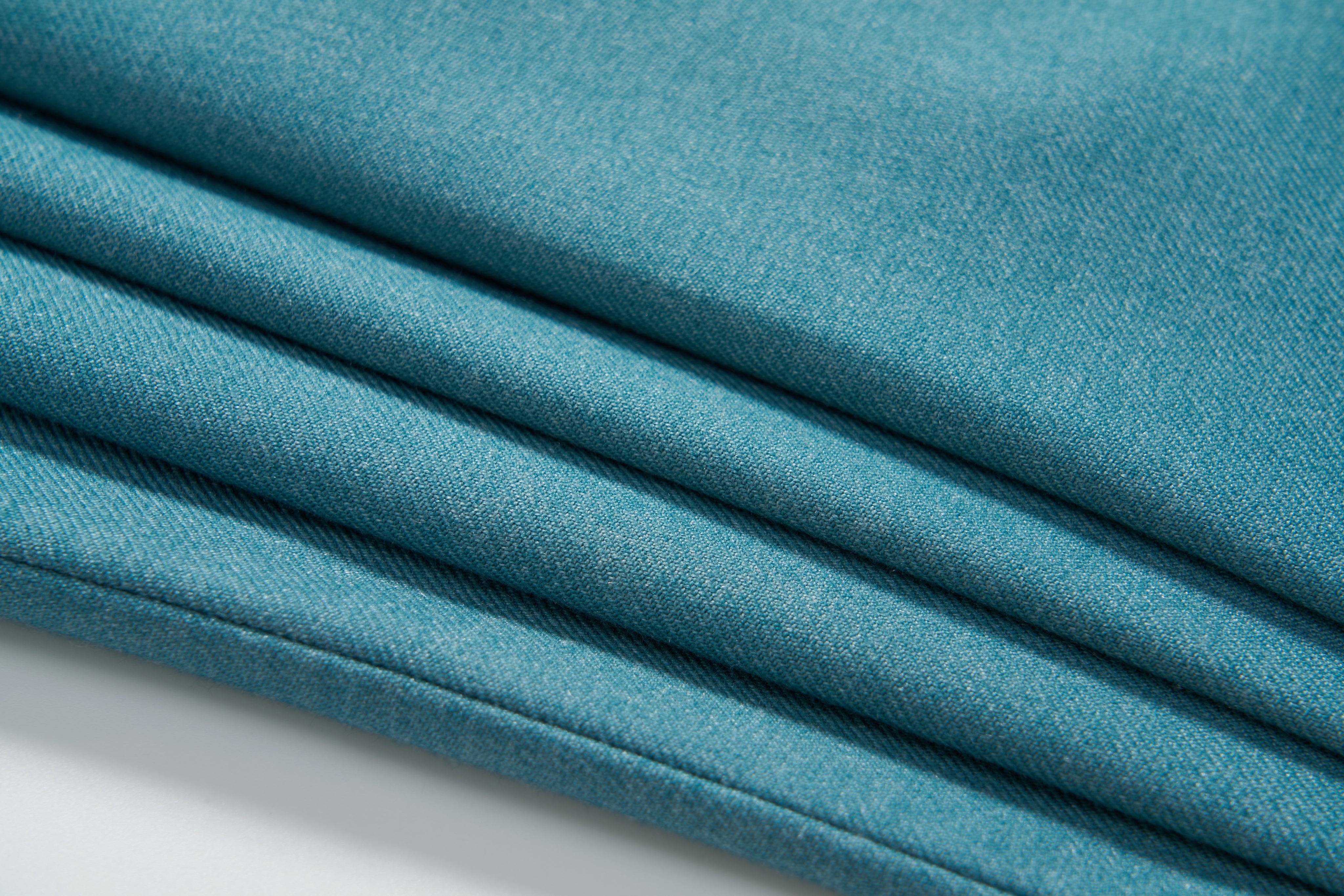 Close-up of four neatly folded layers of turquoise fabric with a smooth texture for KIKI and JOJO's Celeste Whimsy Suit Pants, ideal for boys featuring an adjustable waistband, displayed on a white surface.