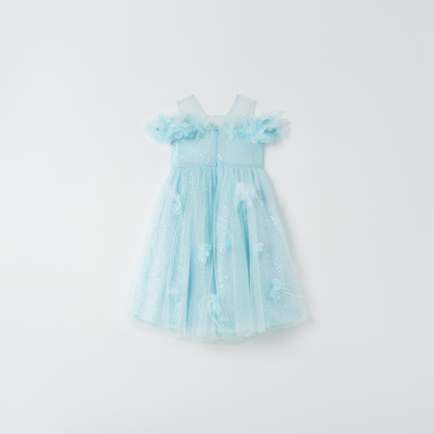 The Feathered Whisper Dress - Blue by KIKI and JOJO is a light blue, sleeveless, knee-length dress with a tulle skirt and floral appliqué, radiating ethereal elegance against a plain white background.