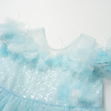 The Feathered Whisper Dress - Blue by KIKI and JOJO features light blue sequins, feather accents, and sheer floral shoulder details, displayed on a white background for an ethereal, elegant look.