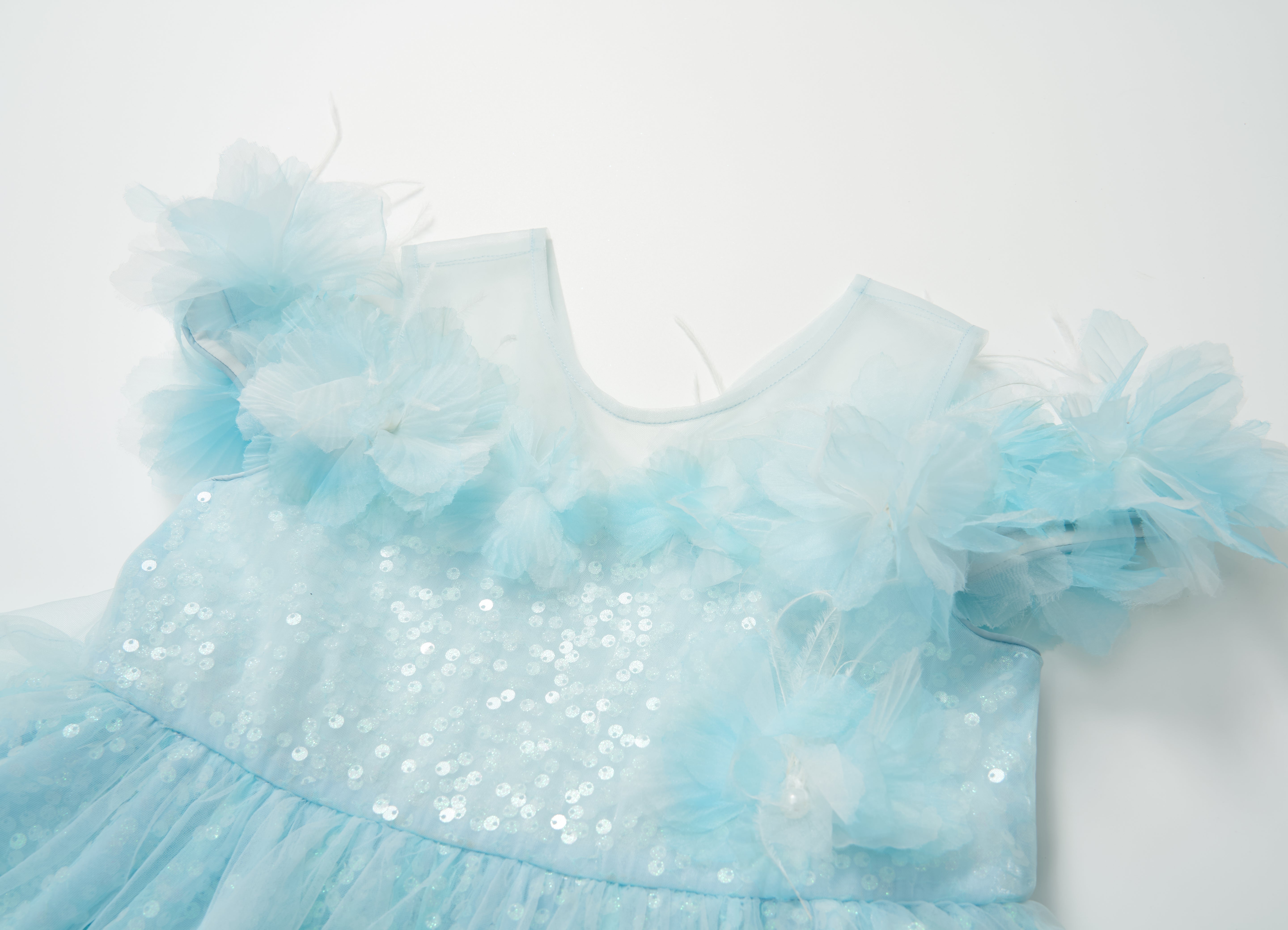 The Feathered Whisper Dress - Blue by KIKI and JOJO features light blue sequins, feather accents, and sheer floral shoulder details, displayed on a white background for an ethereal, elegant look.
