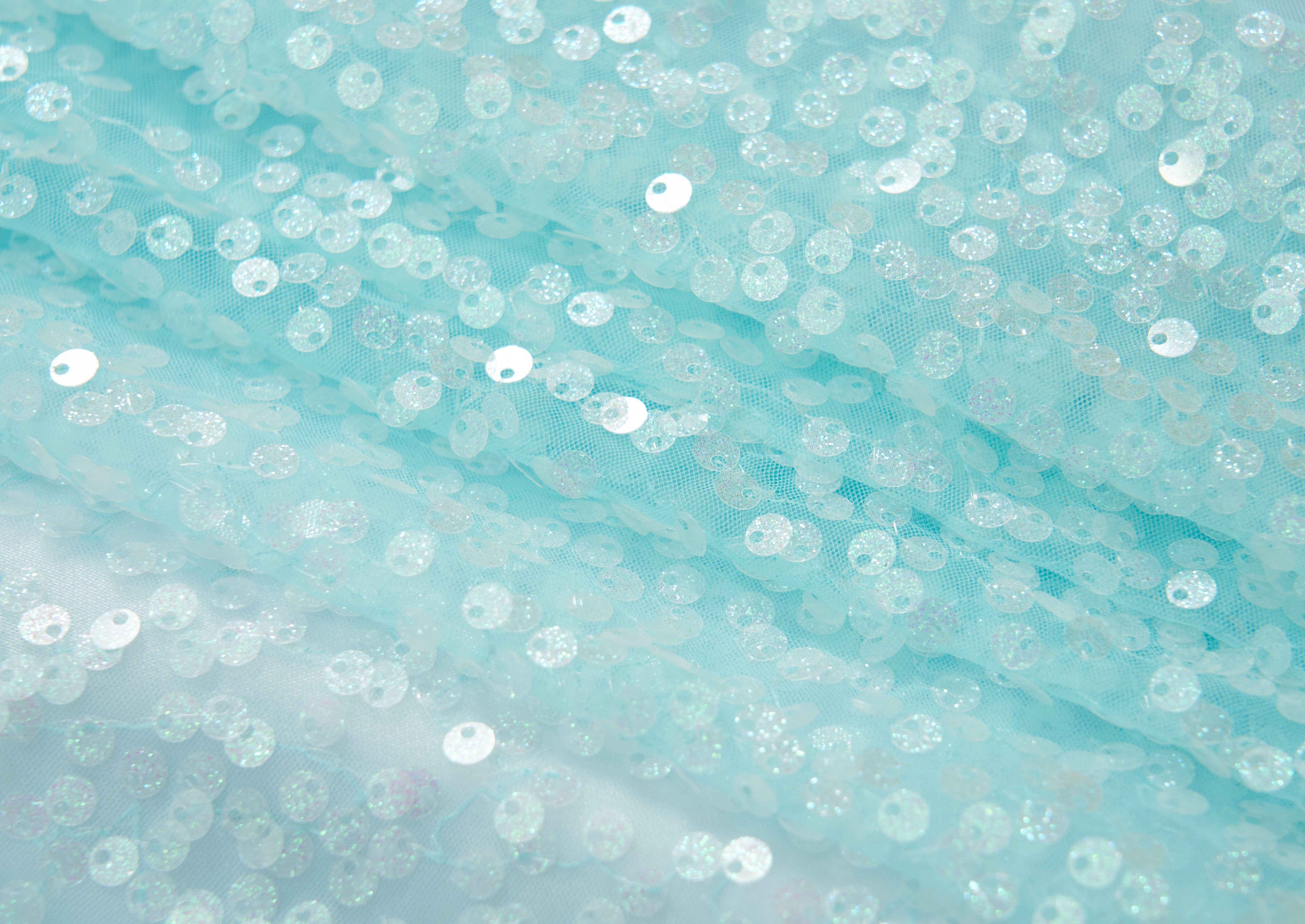 Close-up of the Feathered Whisper Dress - Blue by KIKI and JOJO, featuring pale blue sheer fabric adorned with round iridescent sequins for a shimmering, ethereal look—ideal for an off-shoulder statement.