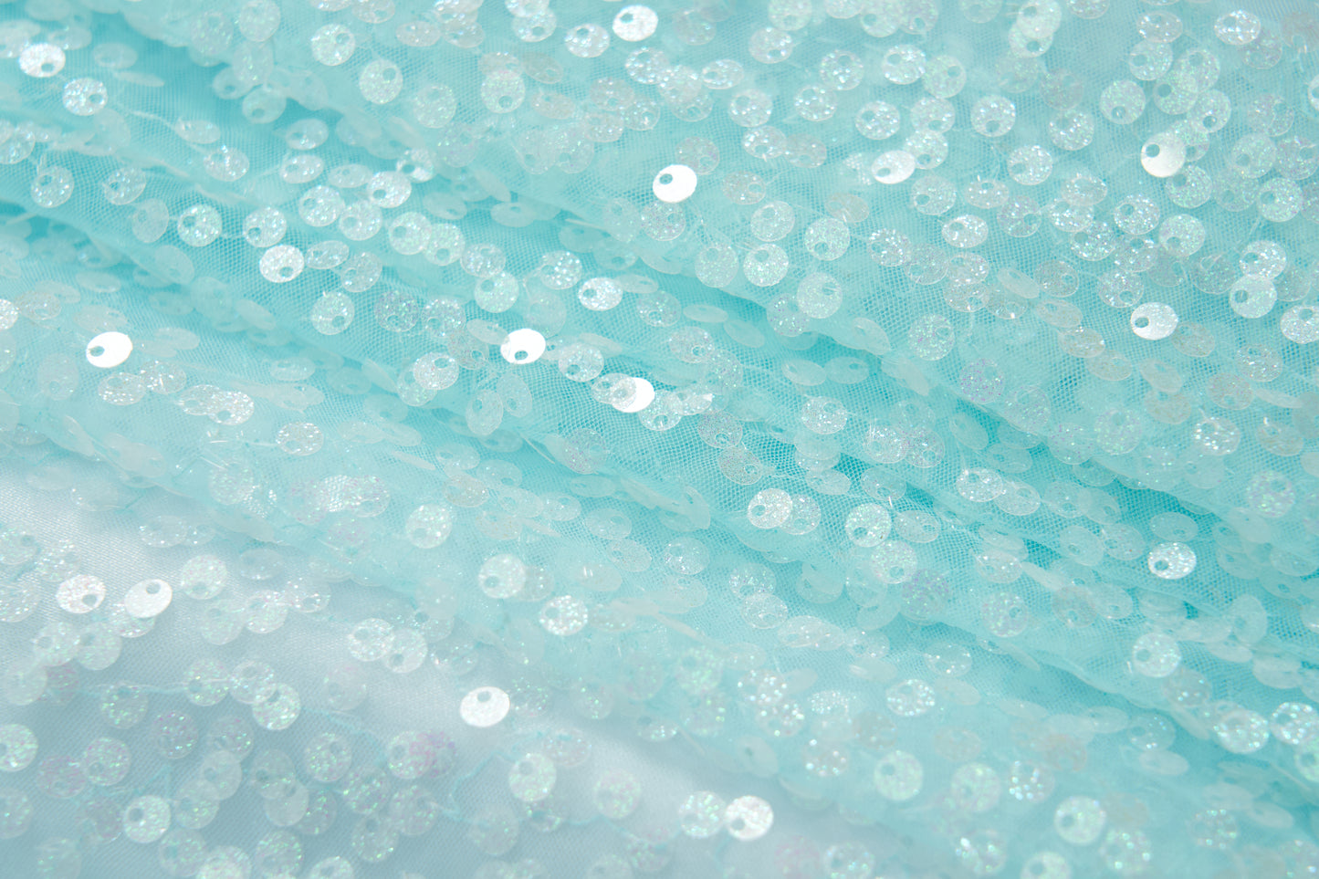 Close-up of the Feathered Whisper Dress - Blue by KIKI and JOJO, featuring pale blue sheer fabric adorned with round iridescent sequins for a shimmering, ethereal look—ideal for an off-shoulder statement.