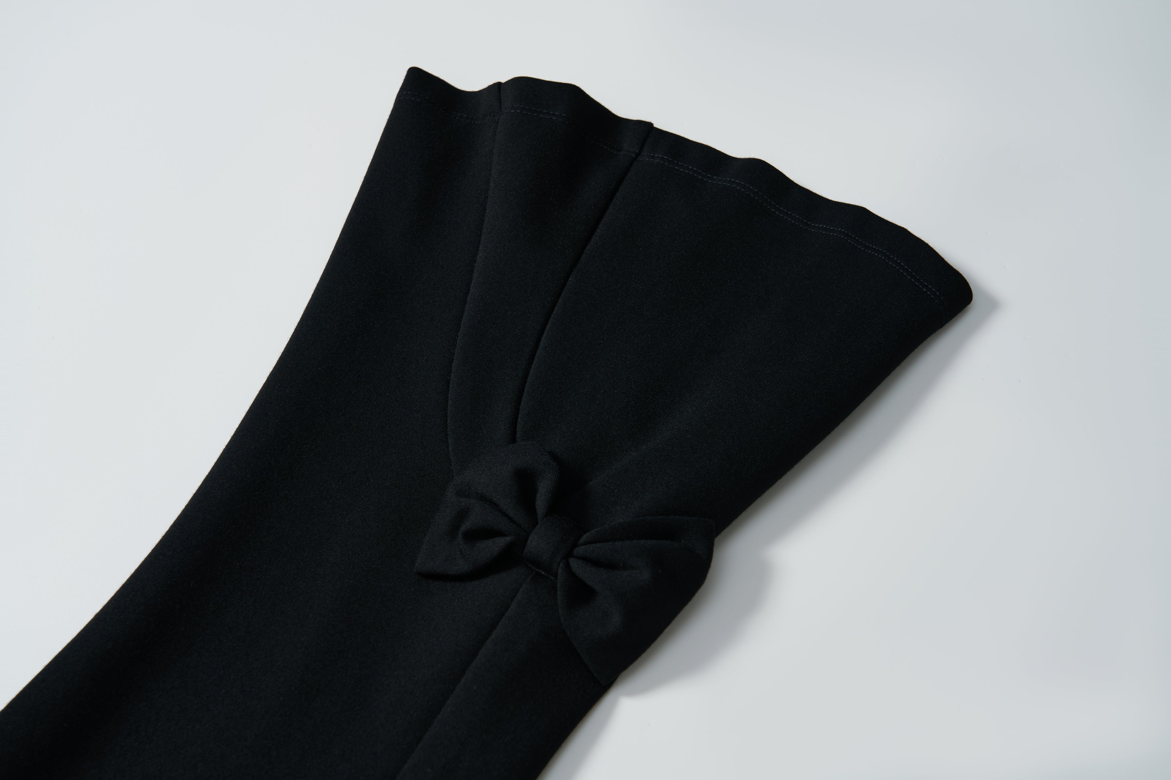 Close-up of the black stretchy sleeve of KIKI and JOJO's Petal Whisper Dress Pants, featuring a small pleat and decorative bow near the cuff, set against a plain white background.